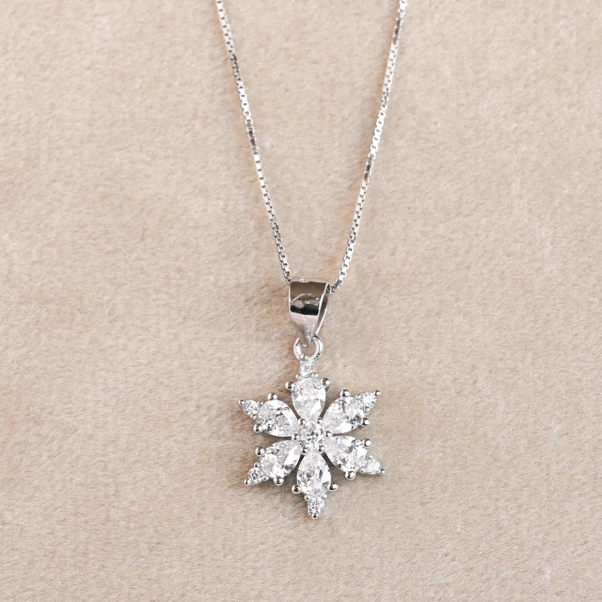 Silver snowflake pendant necklace on a beige background