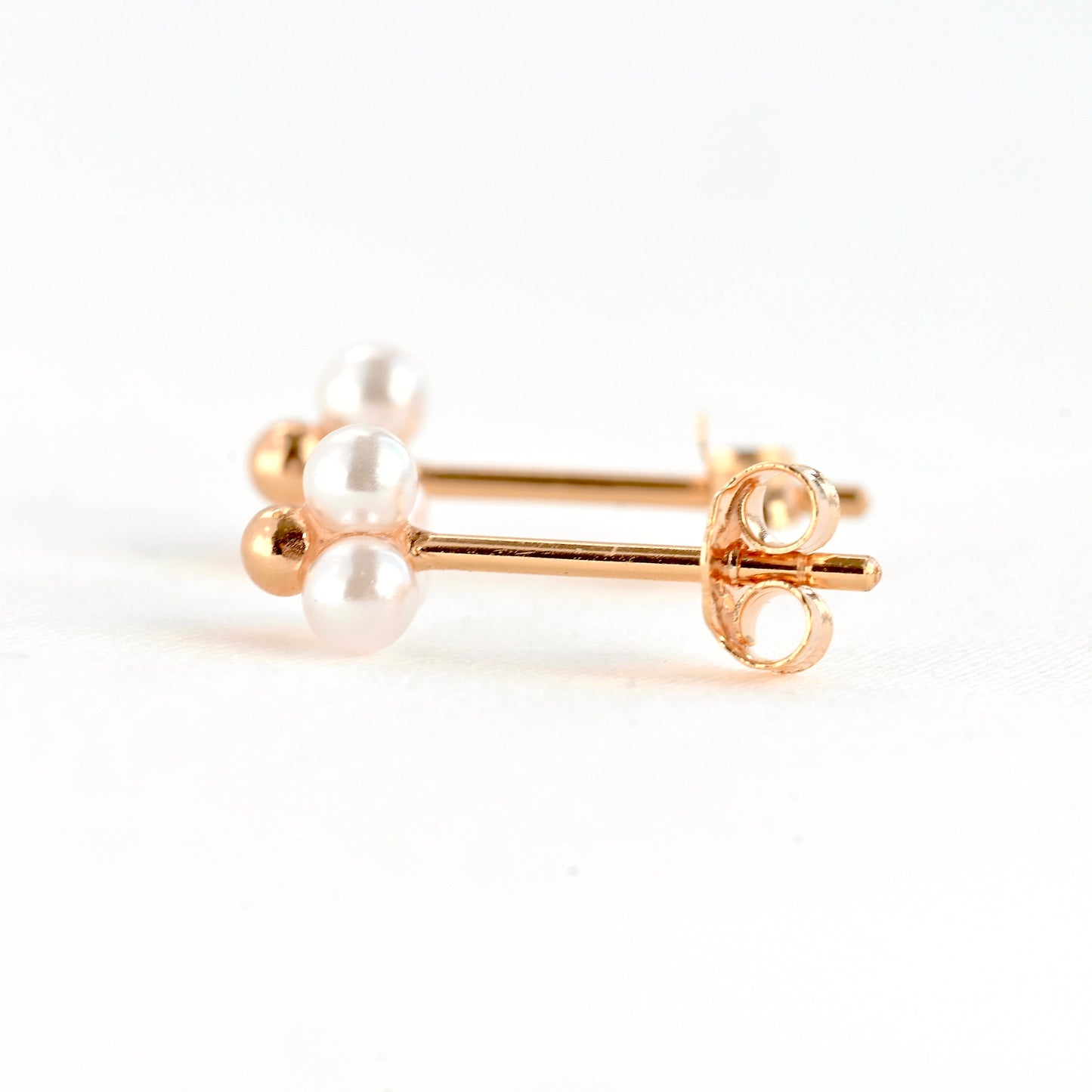 Side view of two rose gold stud earrings with tiny white pearls on a white background