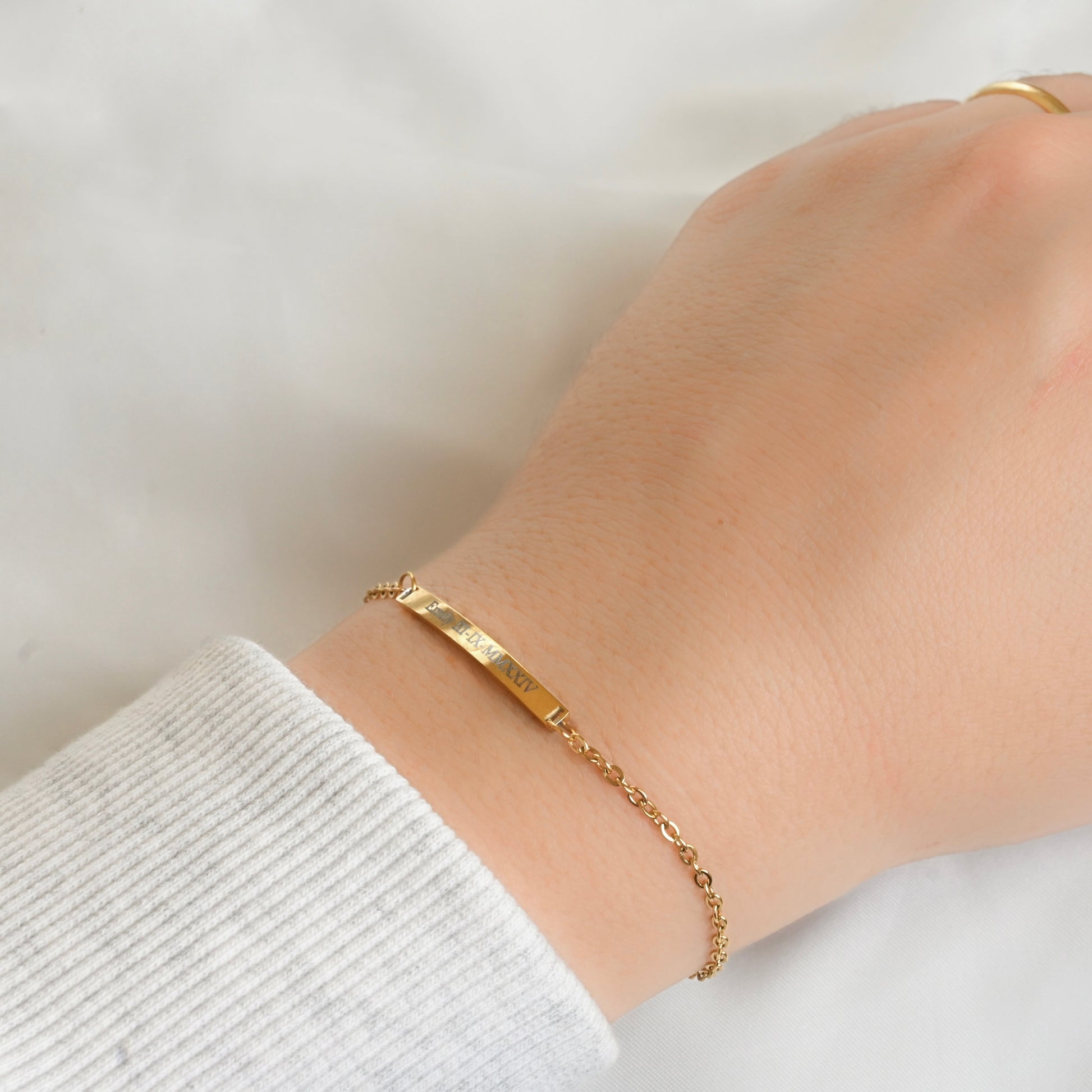 Gold bar bracelet with a small engraved bar and cable chain on a wrist with a white background