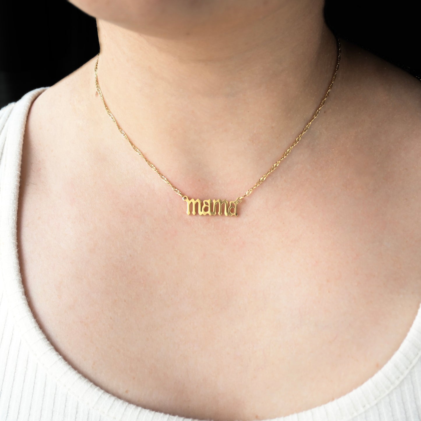 Gold necklace with 'mama' pendant on a singapore chain  on a person wearing a white top.