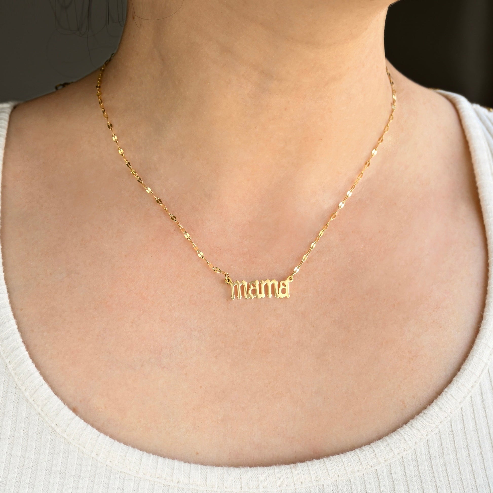 Gold 'mama' necklace on a person wearing a white top