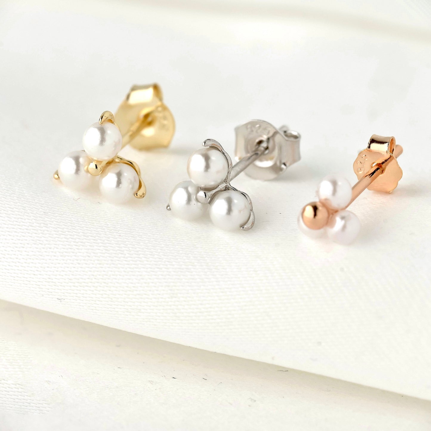 Three pearl cluster earrings in gold, silver, and rose gold on a white background