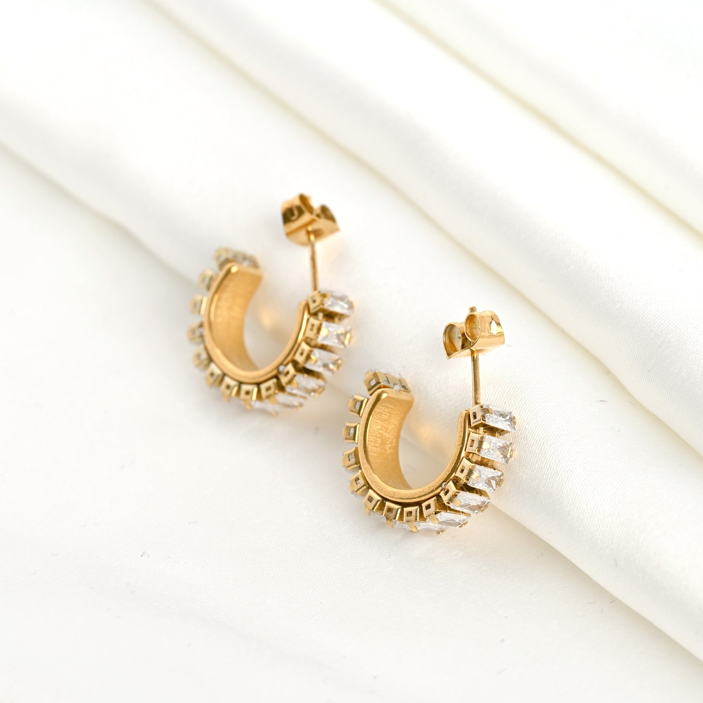 Thick gold hoop earrings with embedded baguette stones on a light background