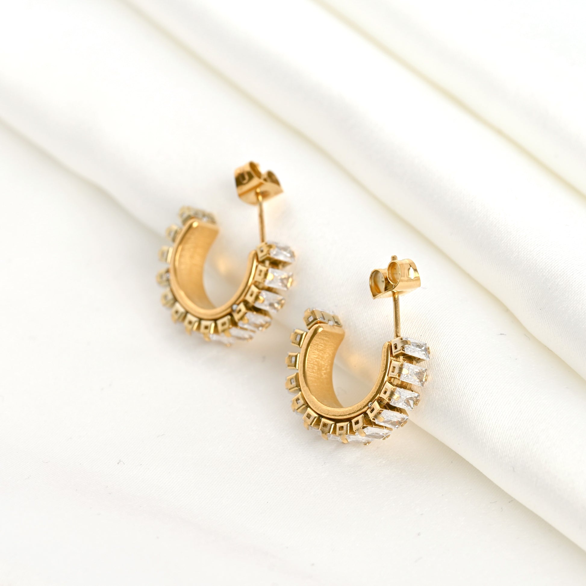 Thick gold hoop earrings with embedded baguette stones on a light background