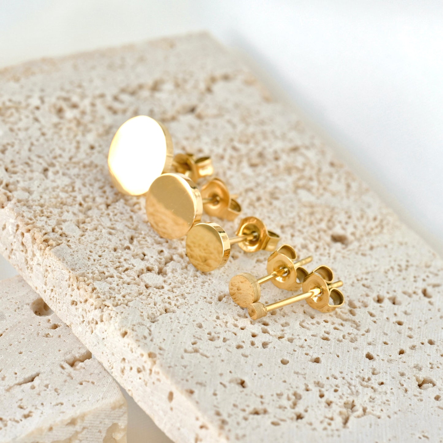 Gold earrings on a textured beige surface