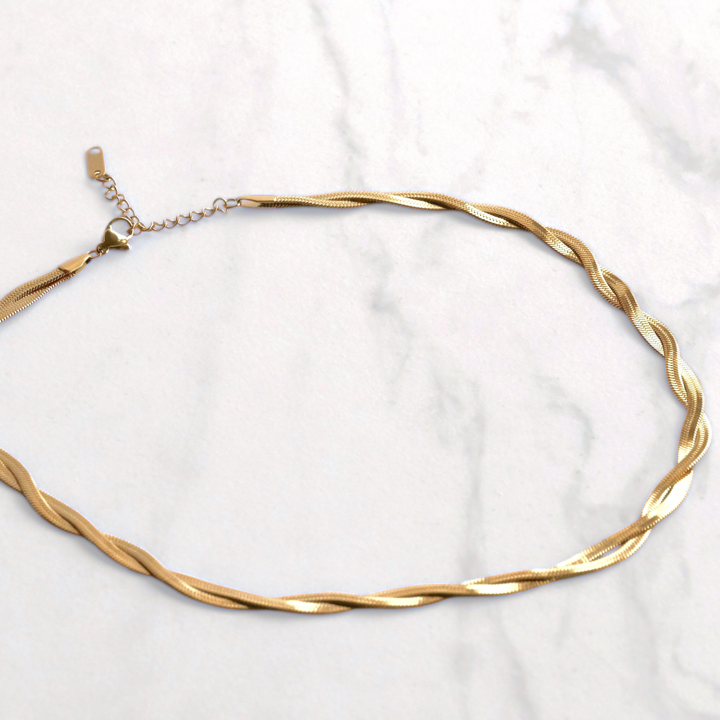 Gold  herringbone necklace on a white marble background
