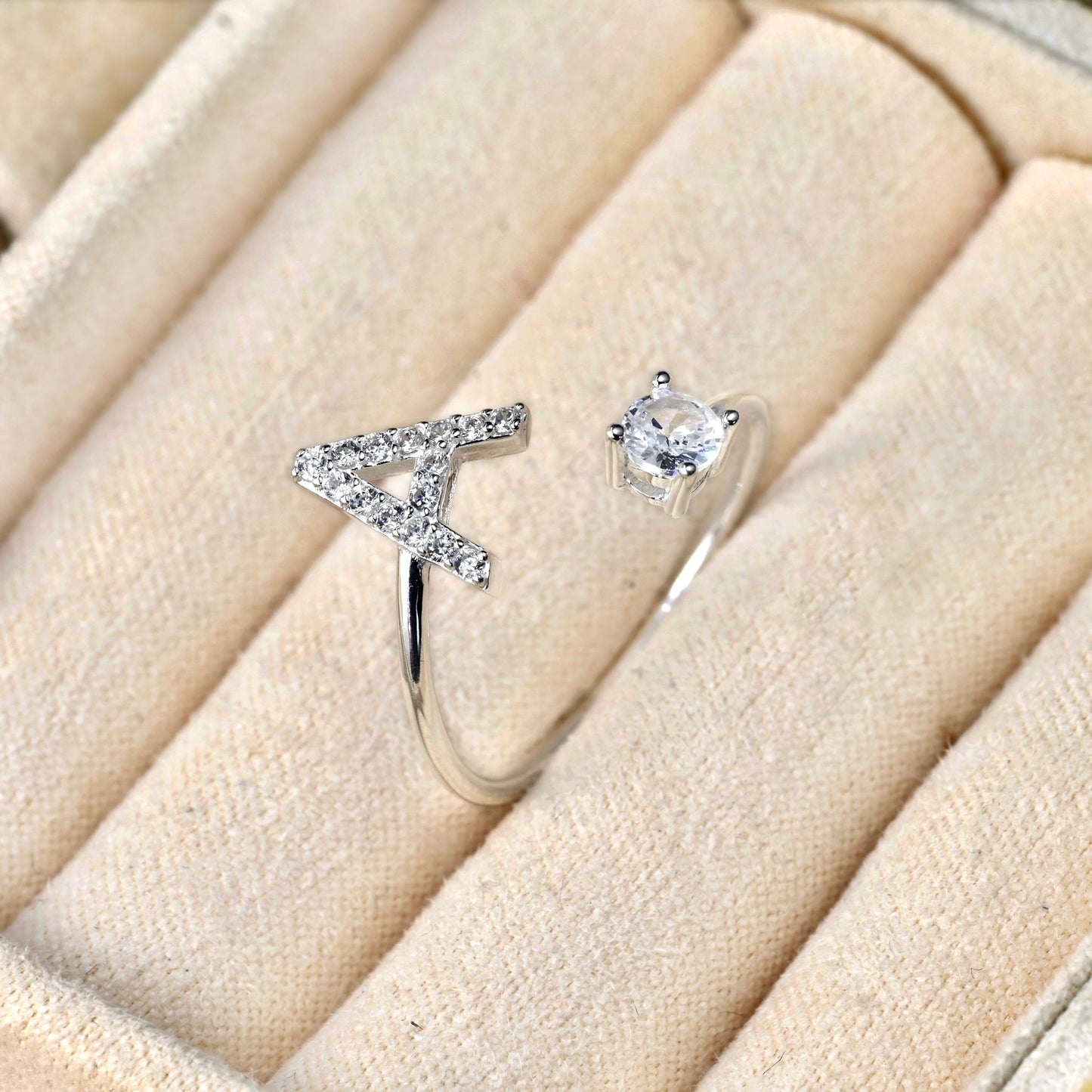 Silver letter ring with a diamond on a beige cushion