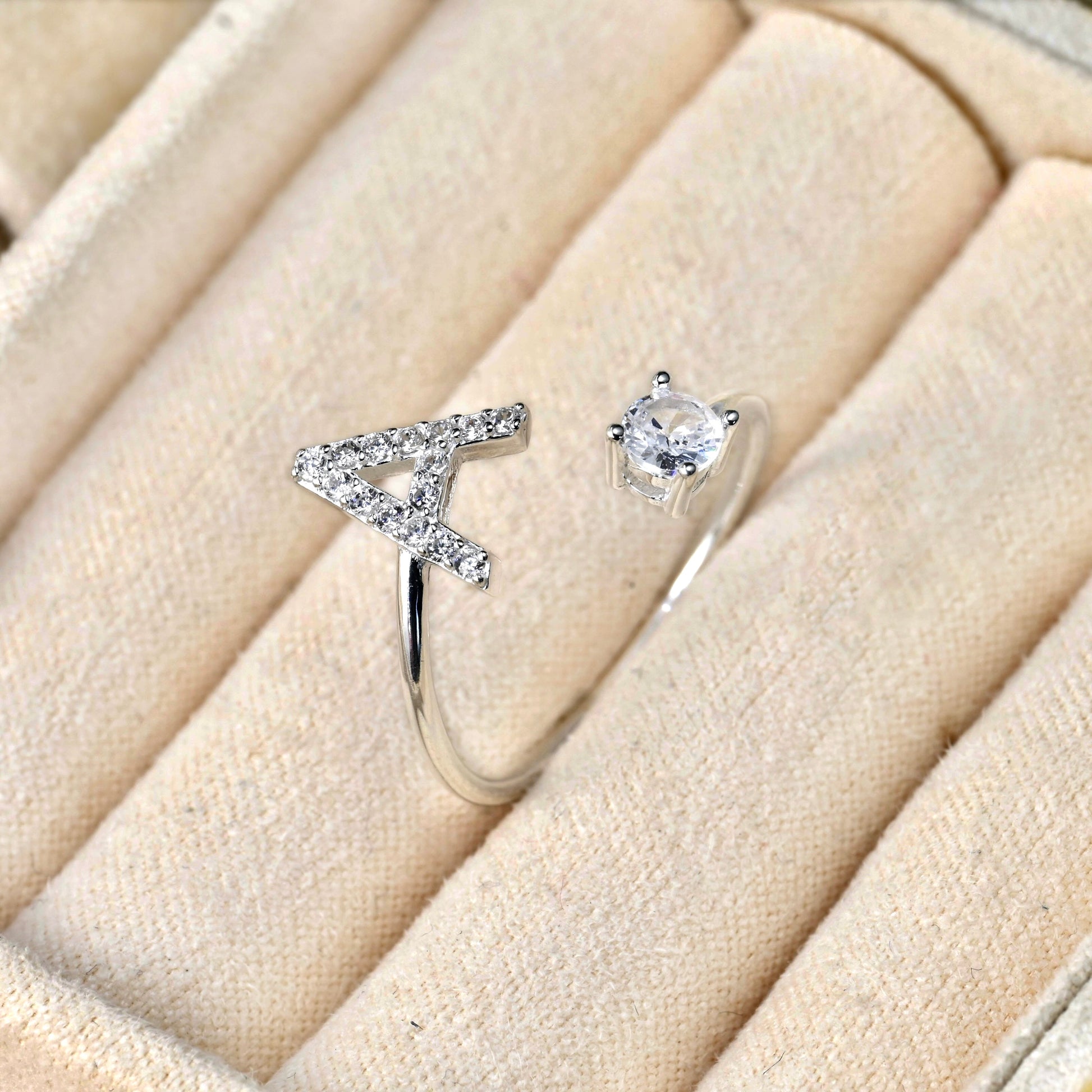 Silver letter ring with a diamond on a beige cushion