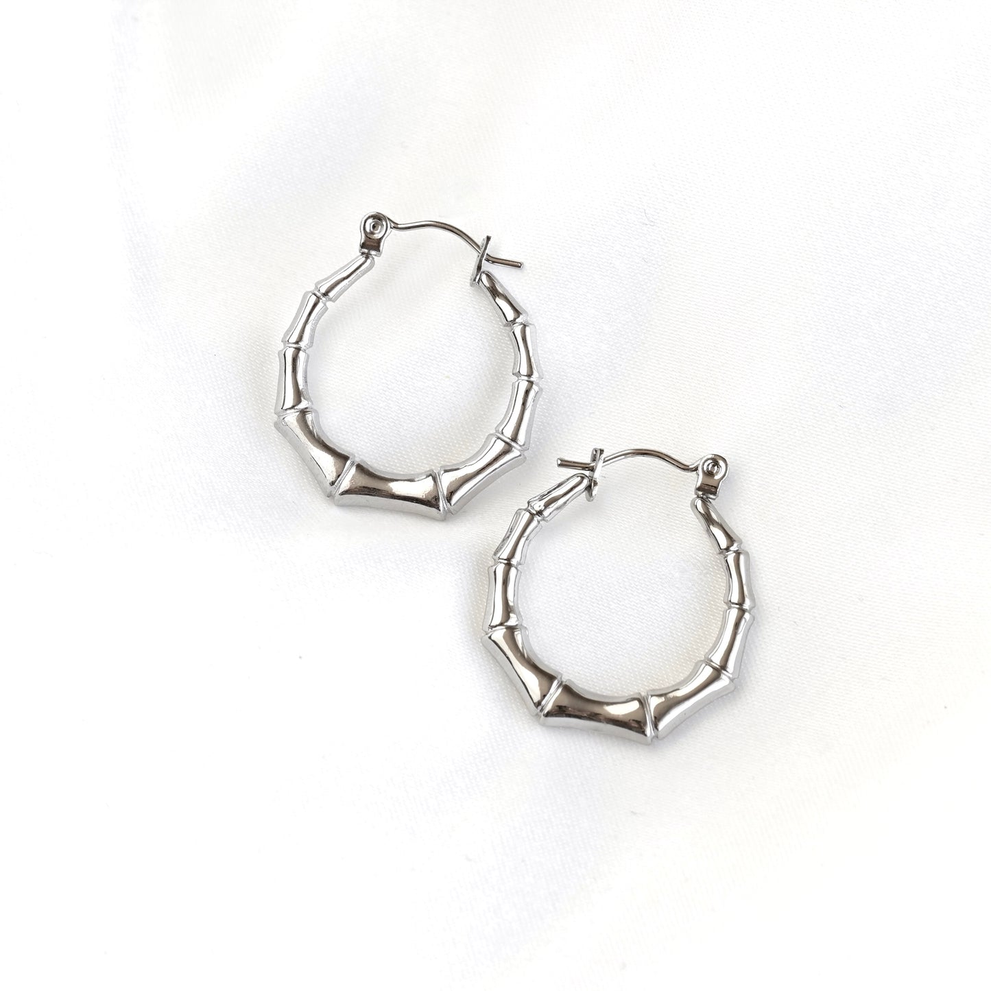 A pair of silver hoop earrings with a textured, segmented design resembling bamboo stalks, displayed on a clean white background.