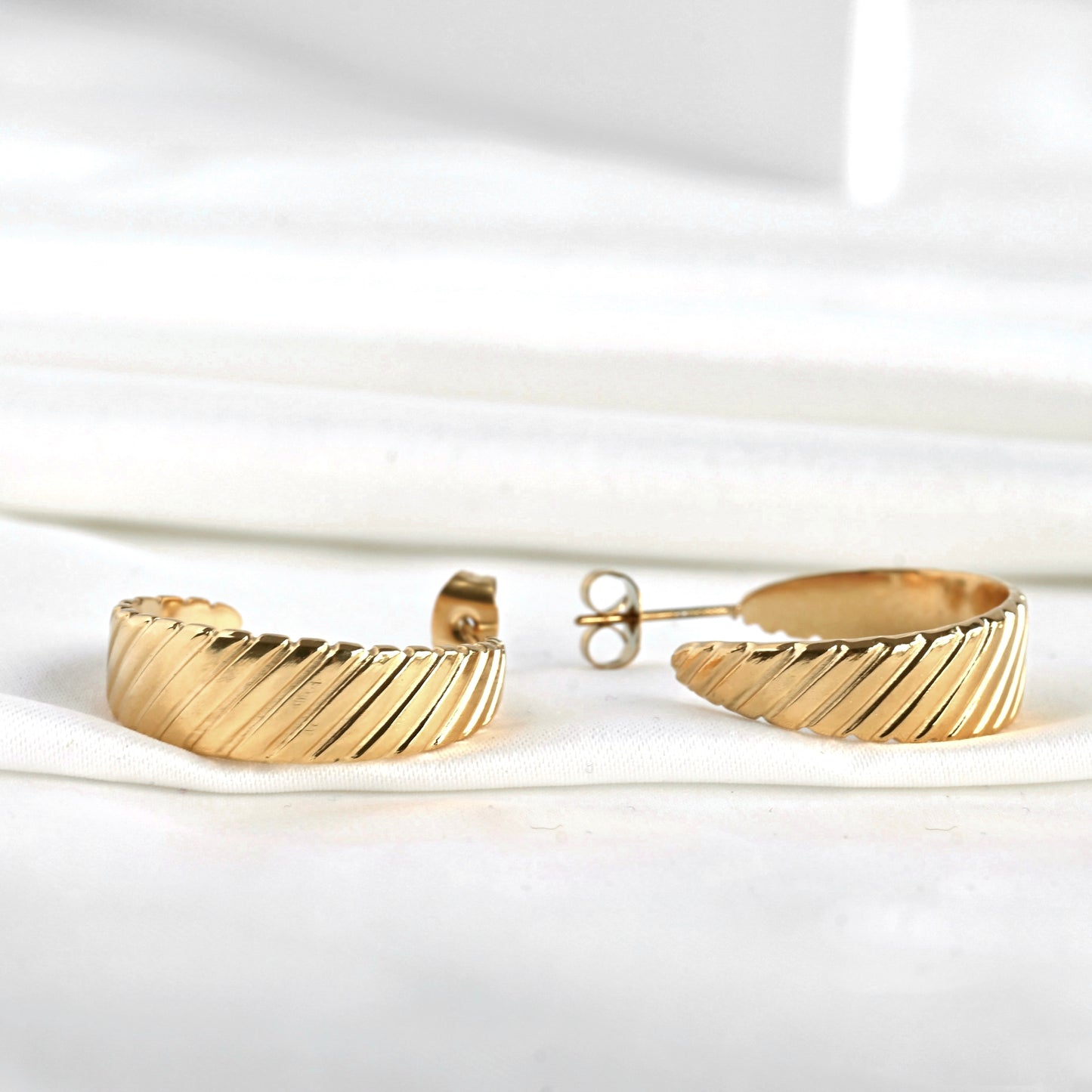 Close-up view of ribbed gold hoop earrings on a white background