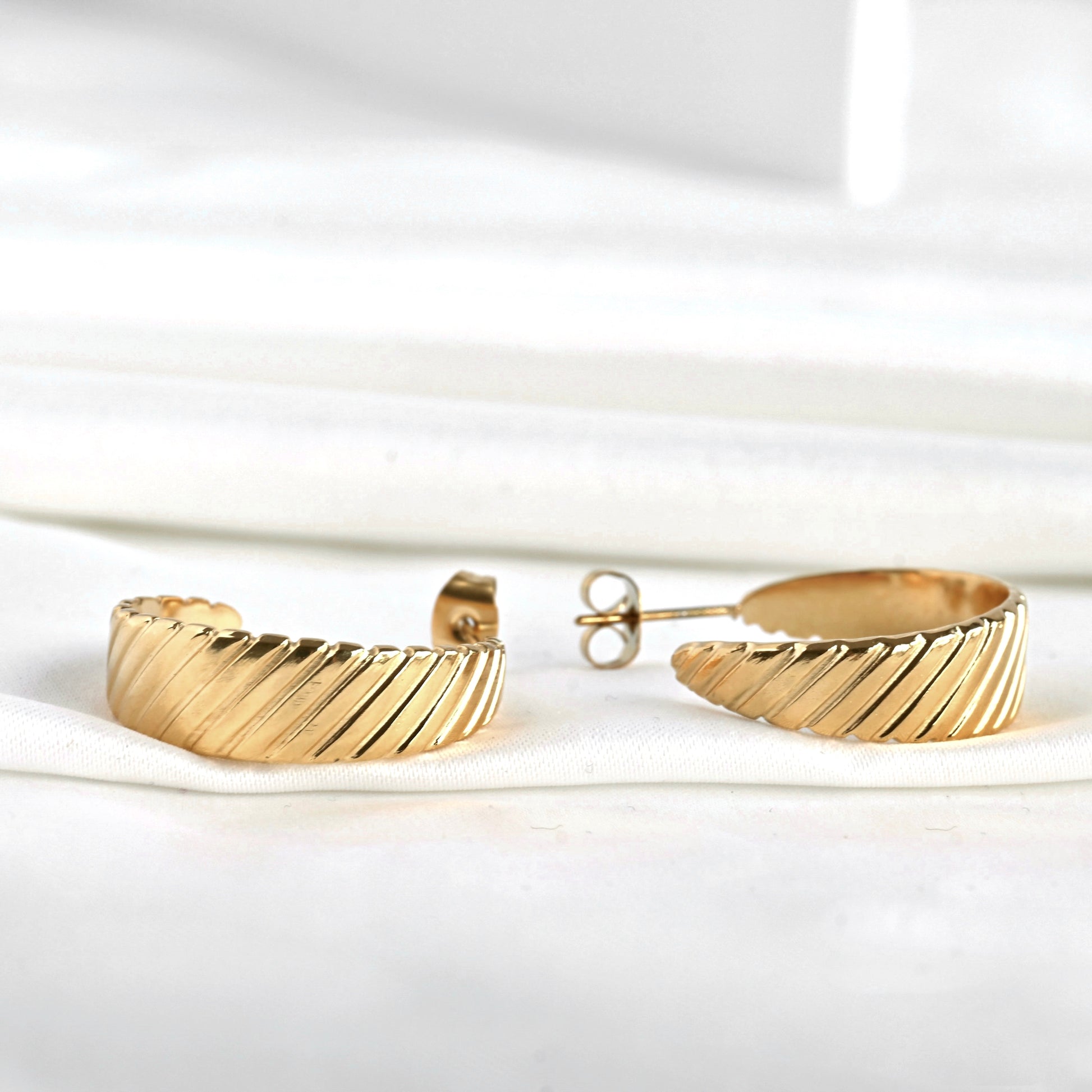Close-up view of ribbed gold hoop earrings on a white background