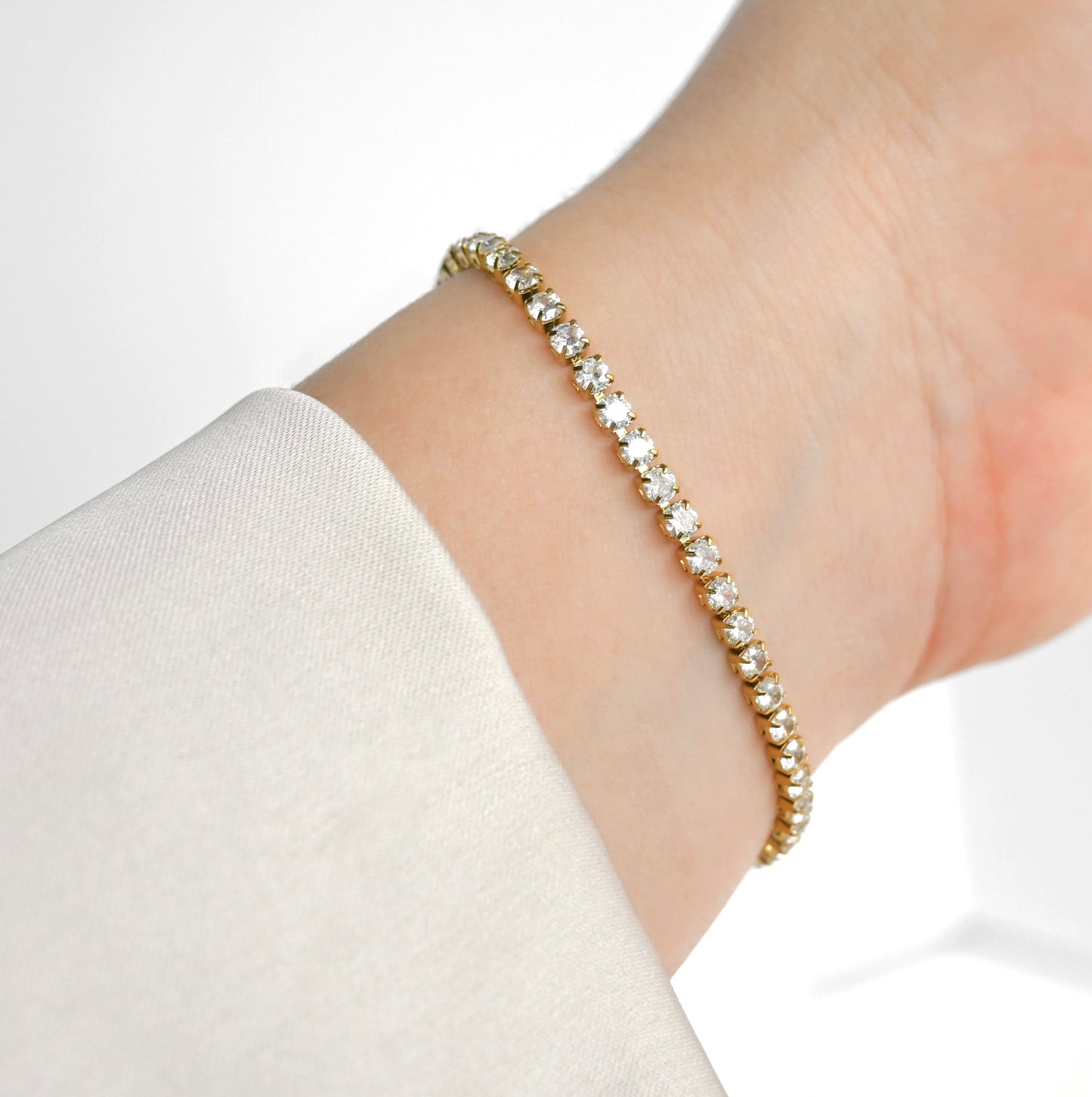 Gold bracelet with clear stones on a wrist against a white background