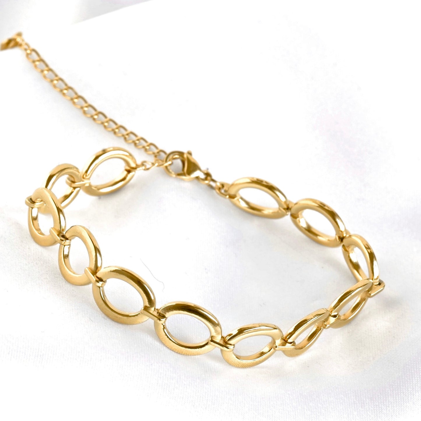 A gold chain bracelet with large, polished oval links, displayed on a clean white fabric background.