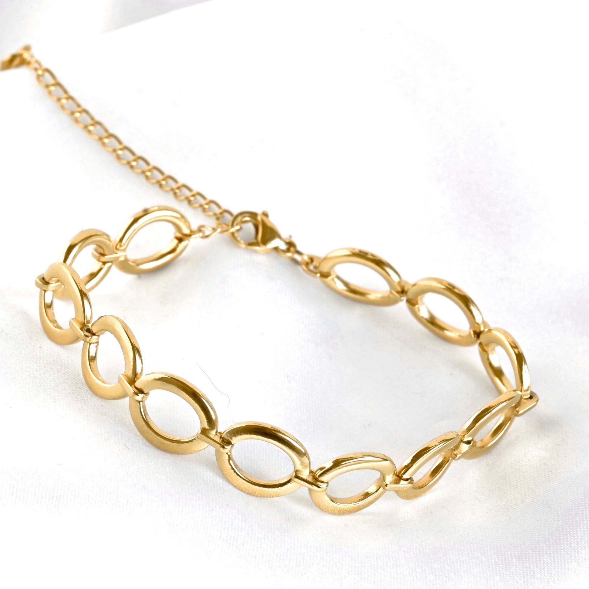 A gold chain bracelet with large, polished oval links, displayed on a clean white fabric background.