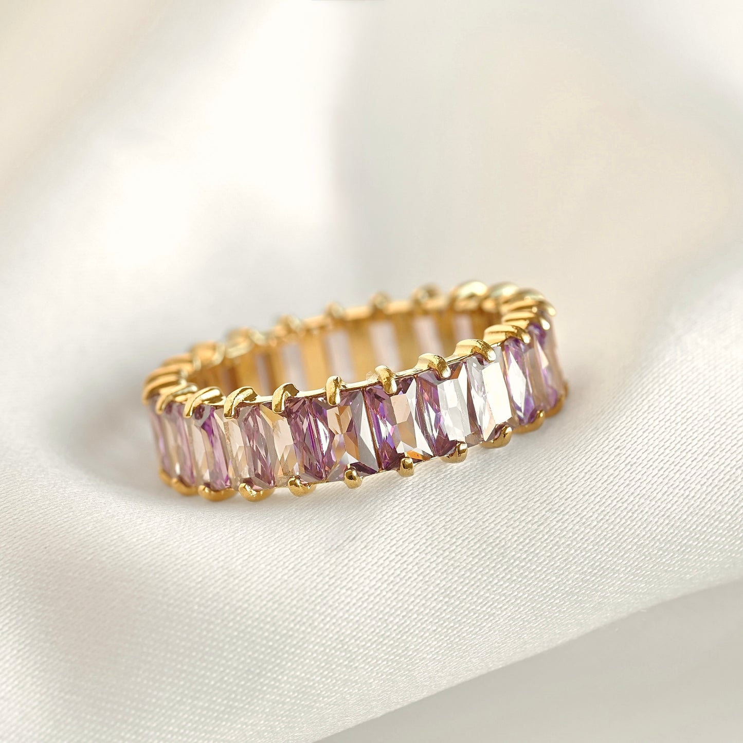 Gold ring with purple gemstones on a white fabric background