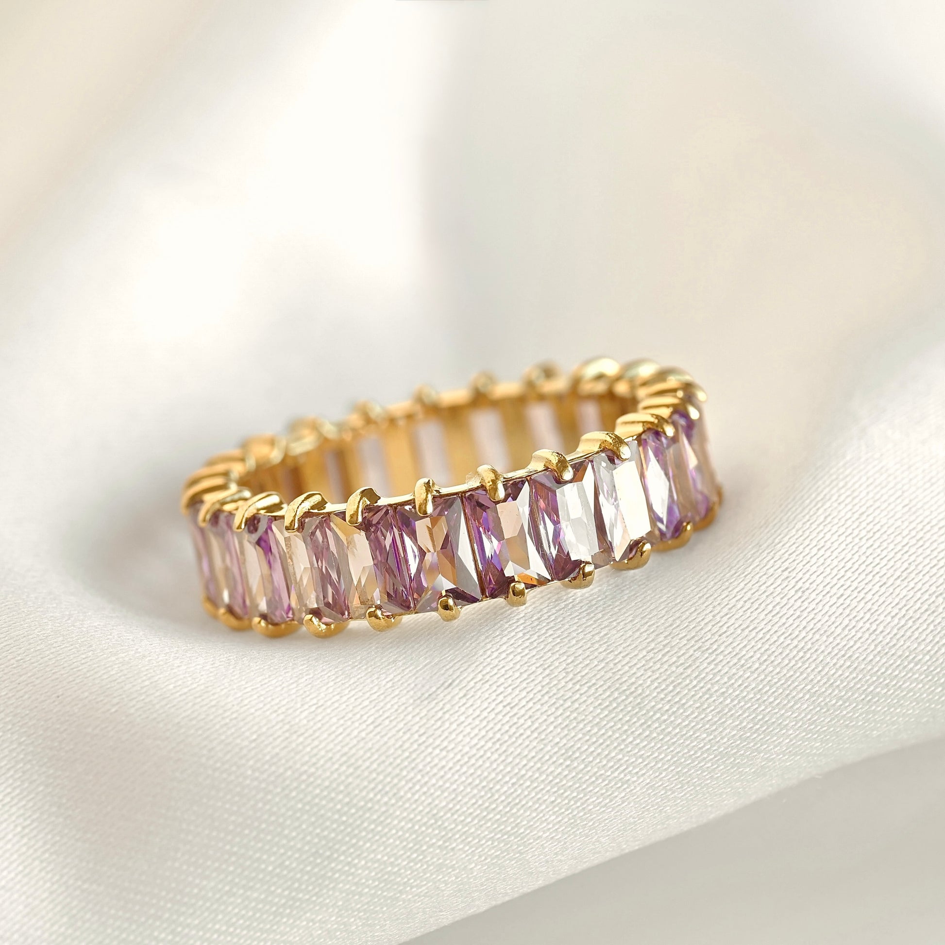 Gold ring with purple gemstones on a white fabric background