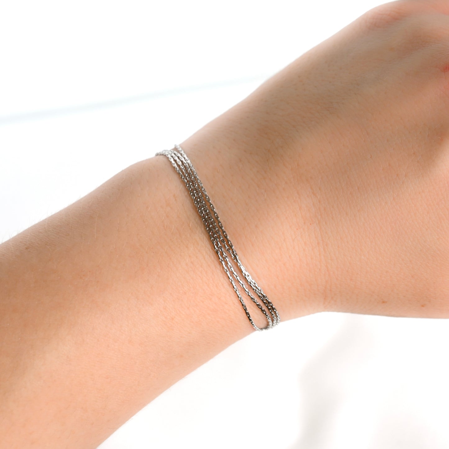 Layered silver sparkle chain bracelet on a wrist against a white background