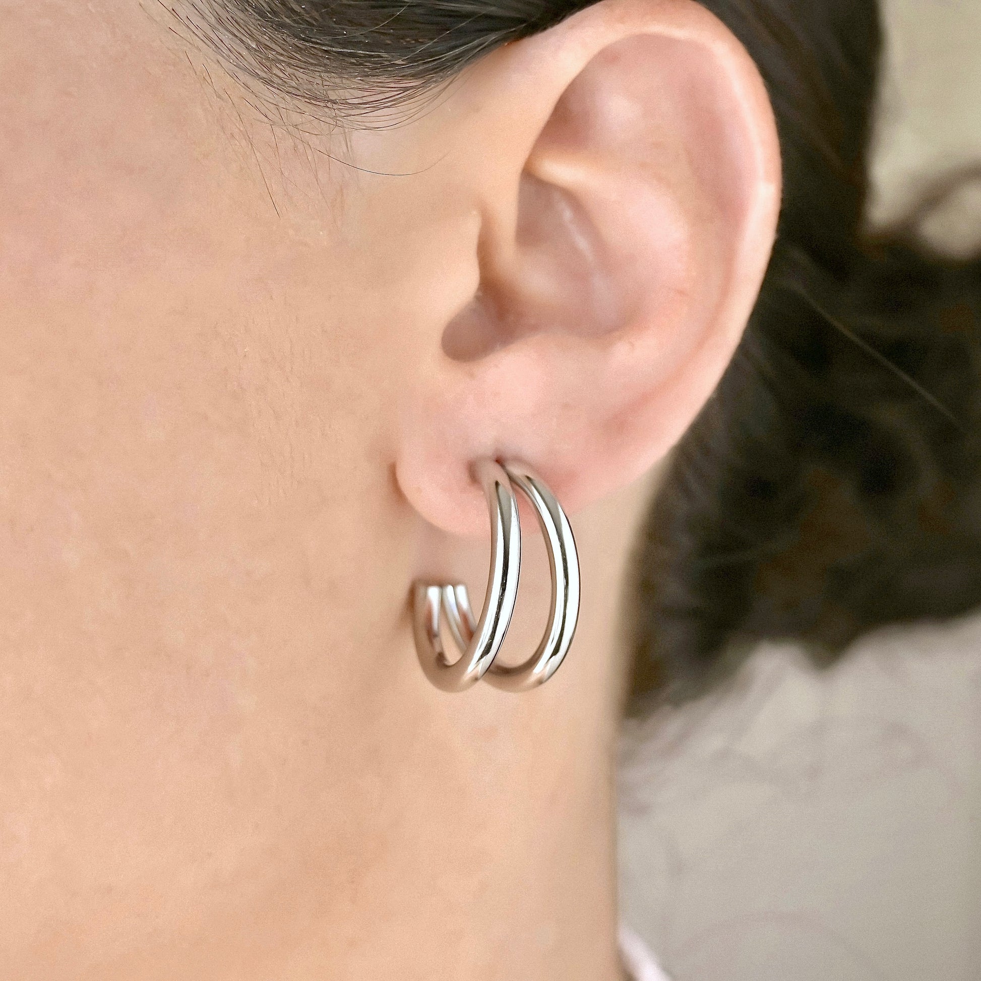 Silver double hoop earrings worn by a person with a neutral background