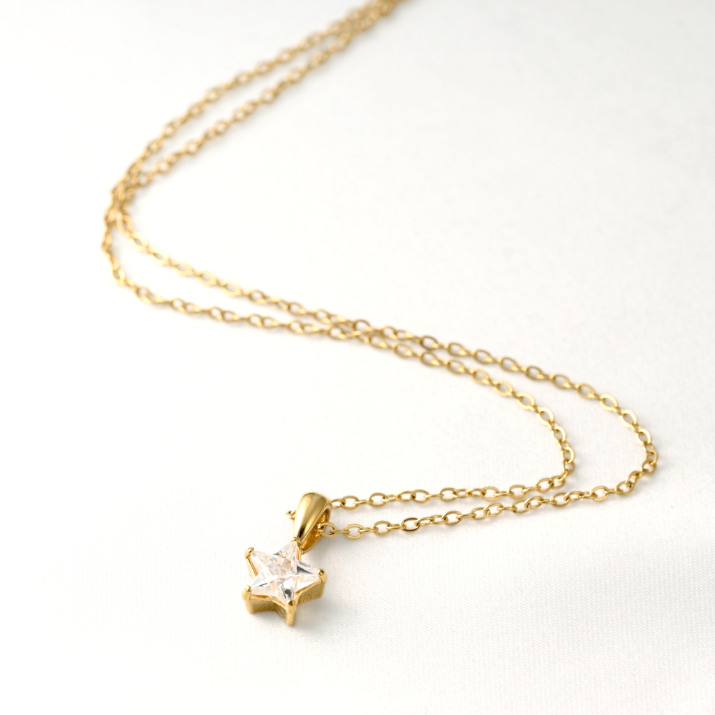 A delicate gold chain necklace with a small gold star pendant featuring a clear, sparkling gemstone, displayed on a clean white background.