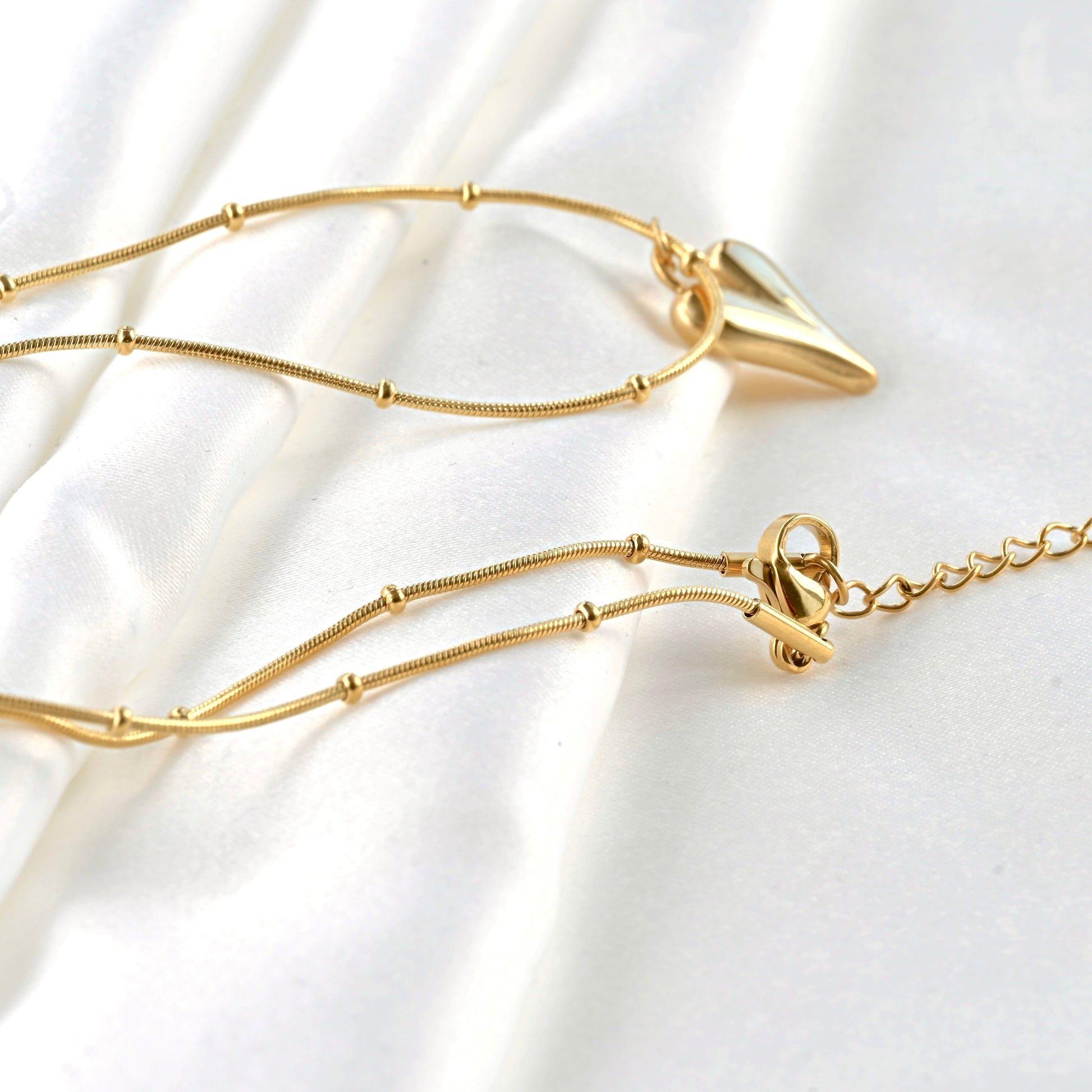 Gold  beaded snake chain necklace with a puffed elongated heart pendant on a white fabric background