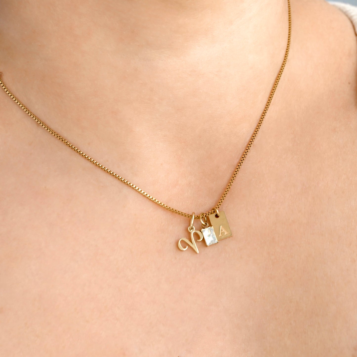 Gold charm necklace with zodiac, baguette stone and rectangular initial charms on a person's neck