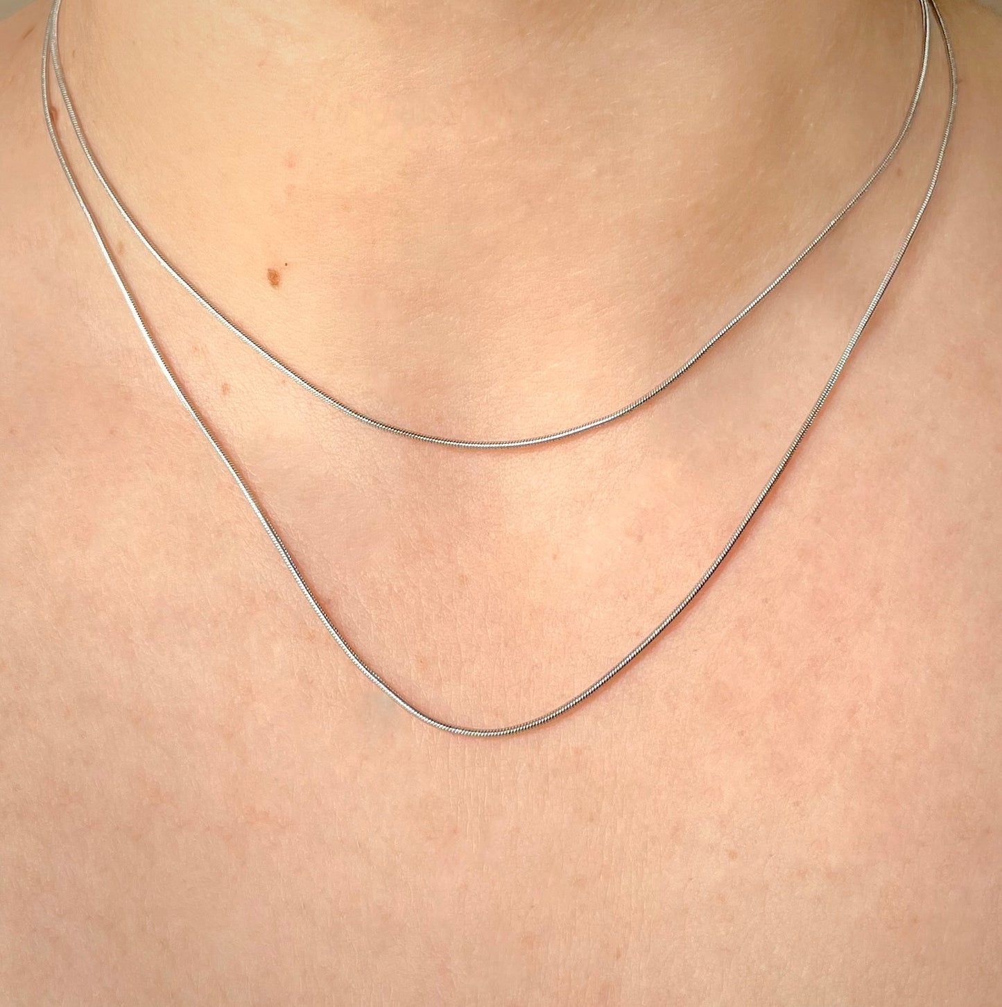 Skinny silver snake necklace set on a person's neck
