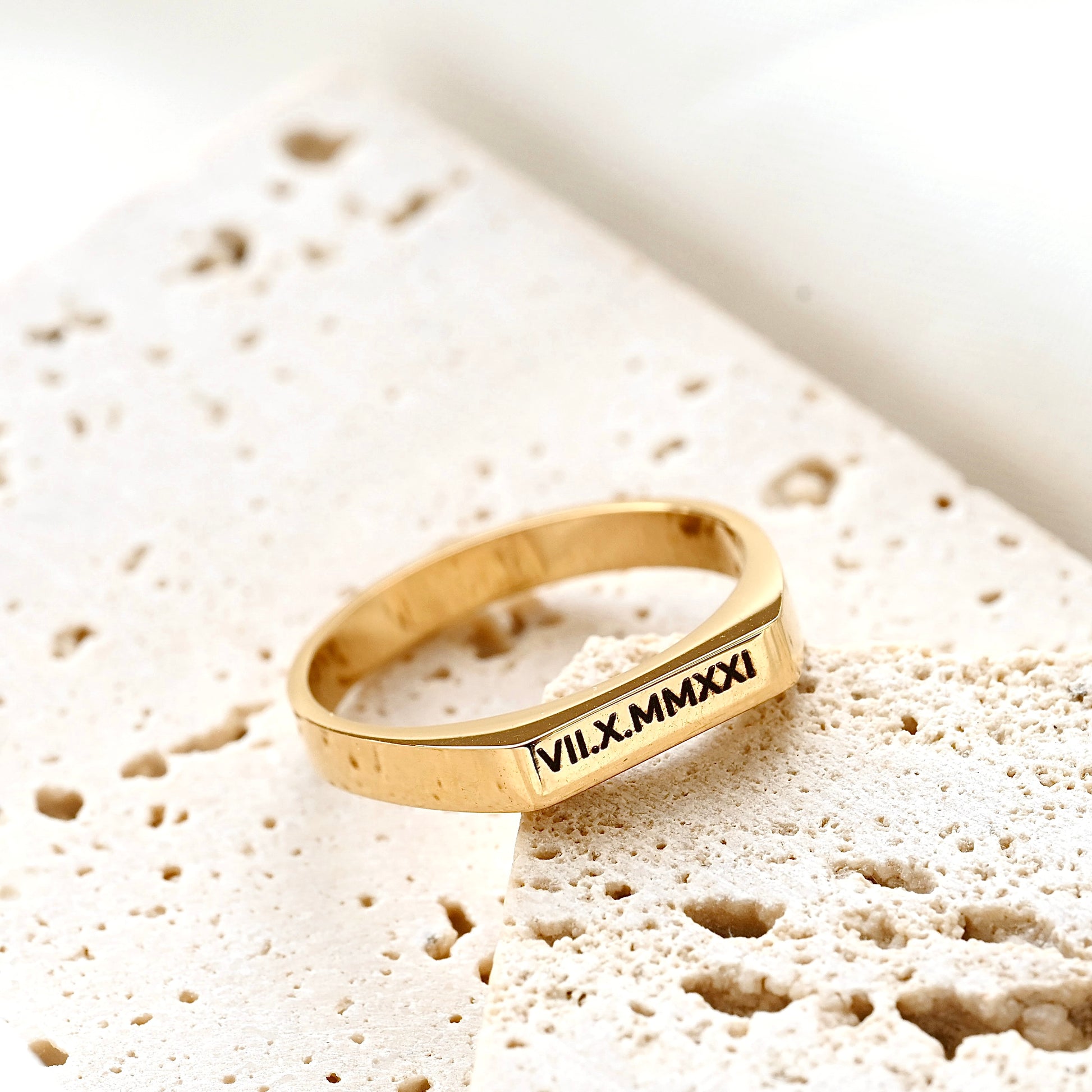 Gold bar ring with engraved Roman numerals on a textured beige stone
