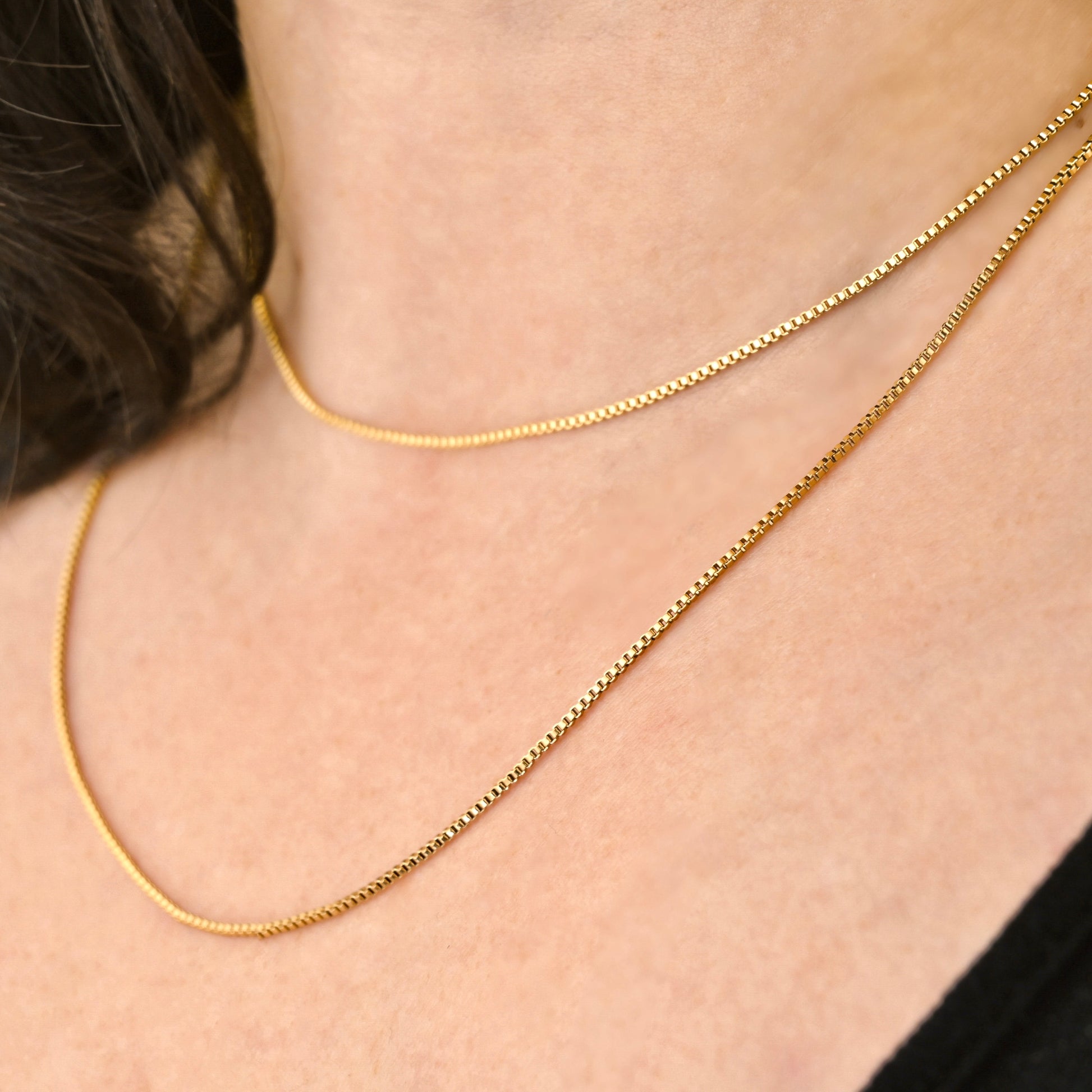 Two gold box chains layered, one long 22 inches, and the other 16 inches, on a person's neck