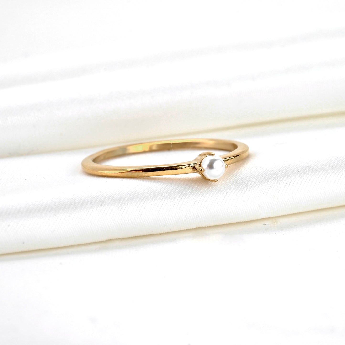 ANgled view of gold ring with a pearl on a white fabric background