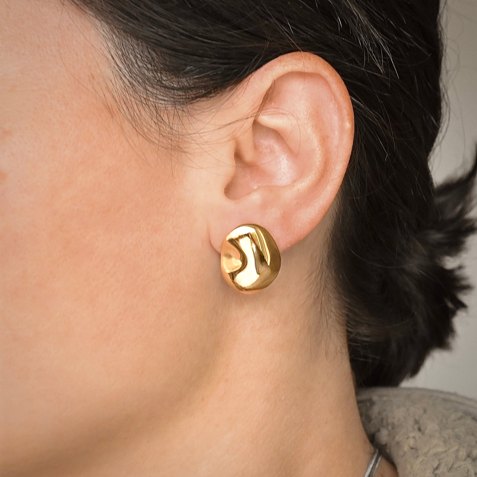 Close-up of an ear wearing sculptural gold earrings with blurred background