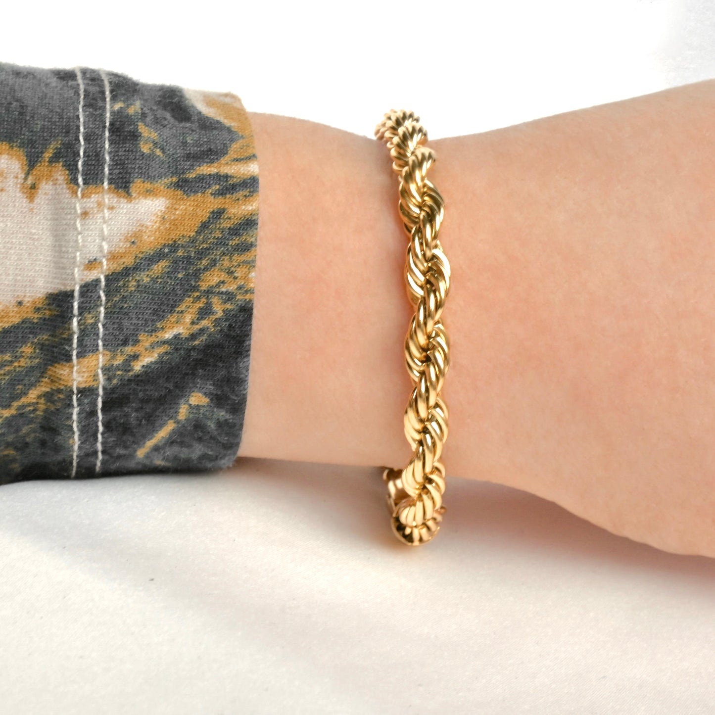 Side view of thick gold rope chain bracelet on a wrist with a neutral background