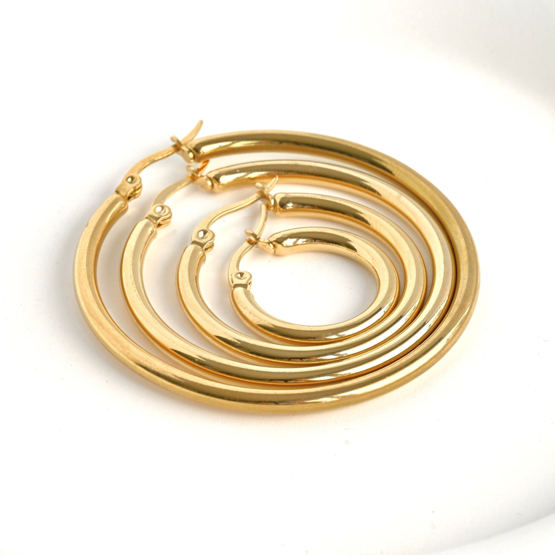 A top-down shot of four nesting gold chunky hoop earrings on a clean white background.