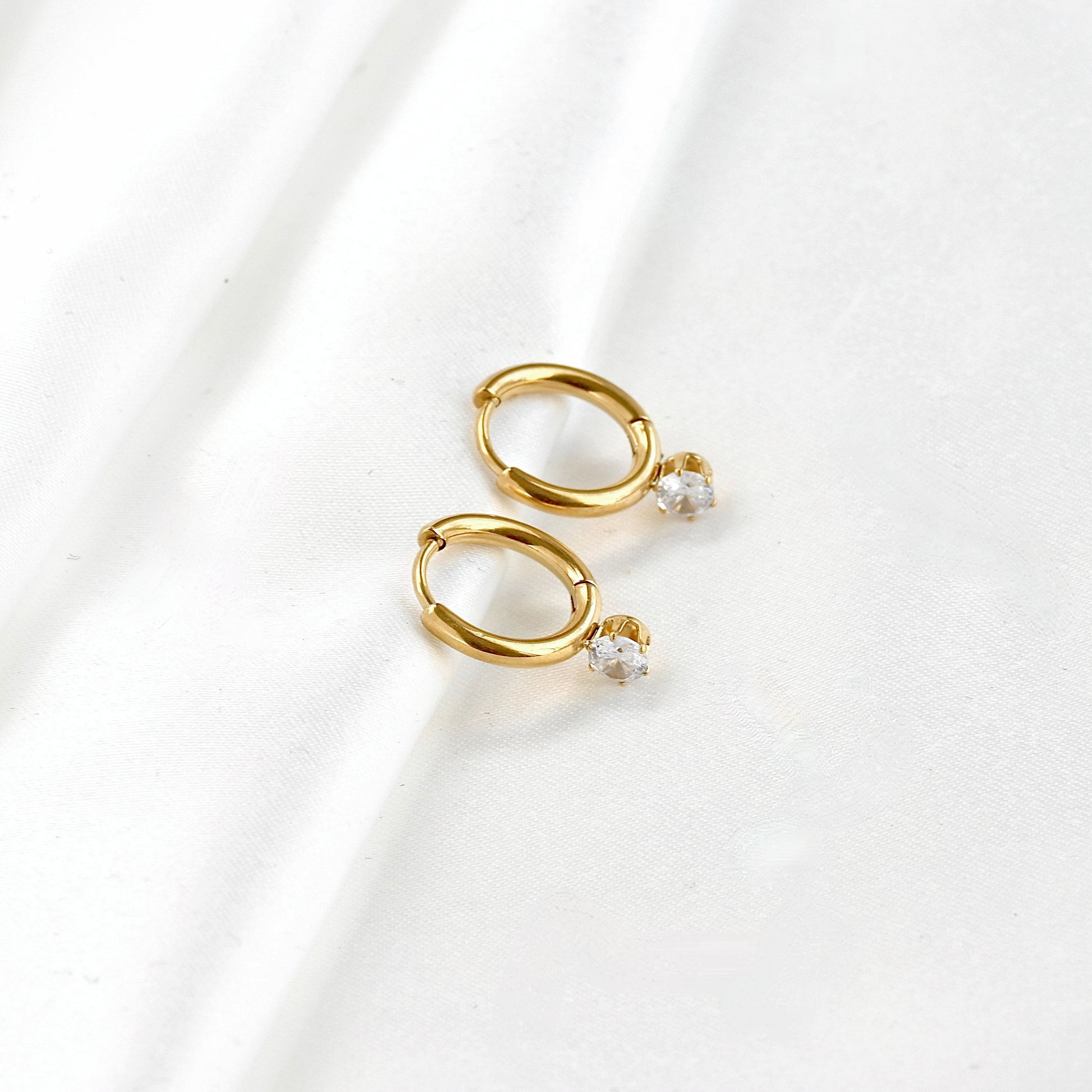 Wide angle view of cubic zirconia attached gold hoop earrings on a white background