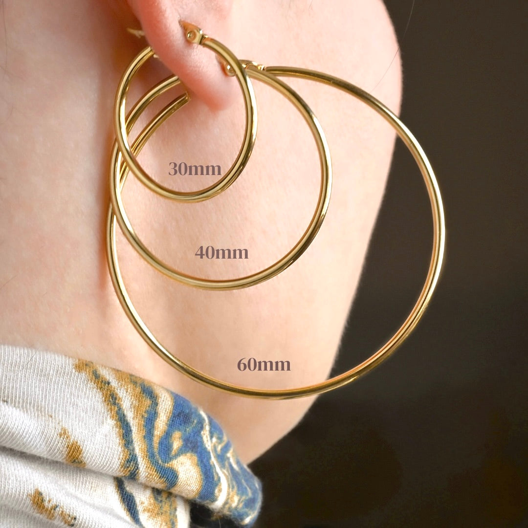 Back view of slim gold hoops in 3 different sizes worn by a person with a dark background with size measurements.