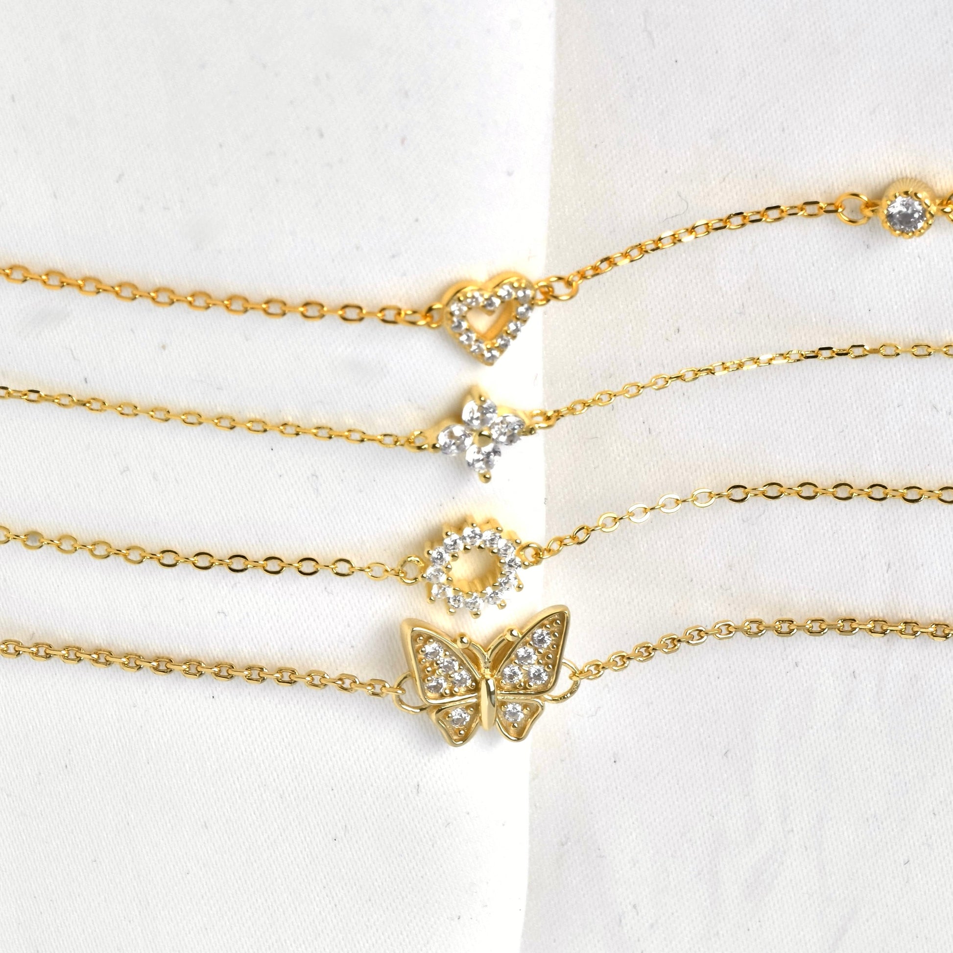 SIde view of gold bracelet set with butterfly, flower and heart chaerms with embedded stones on a white background
