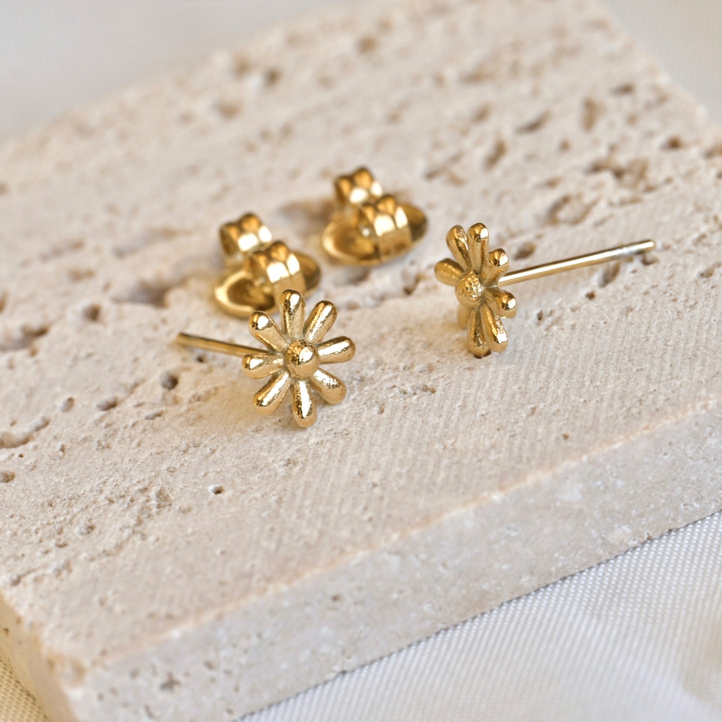 Gold daisy earrings on a textured beige surface