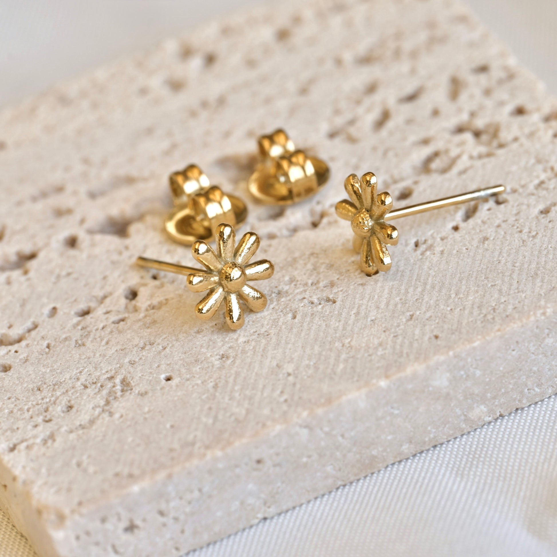 Gold daisy earrings on a textured beige surface