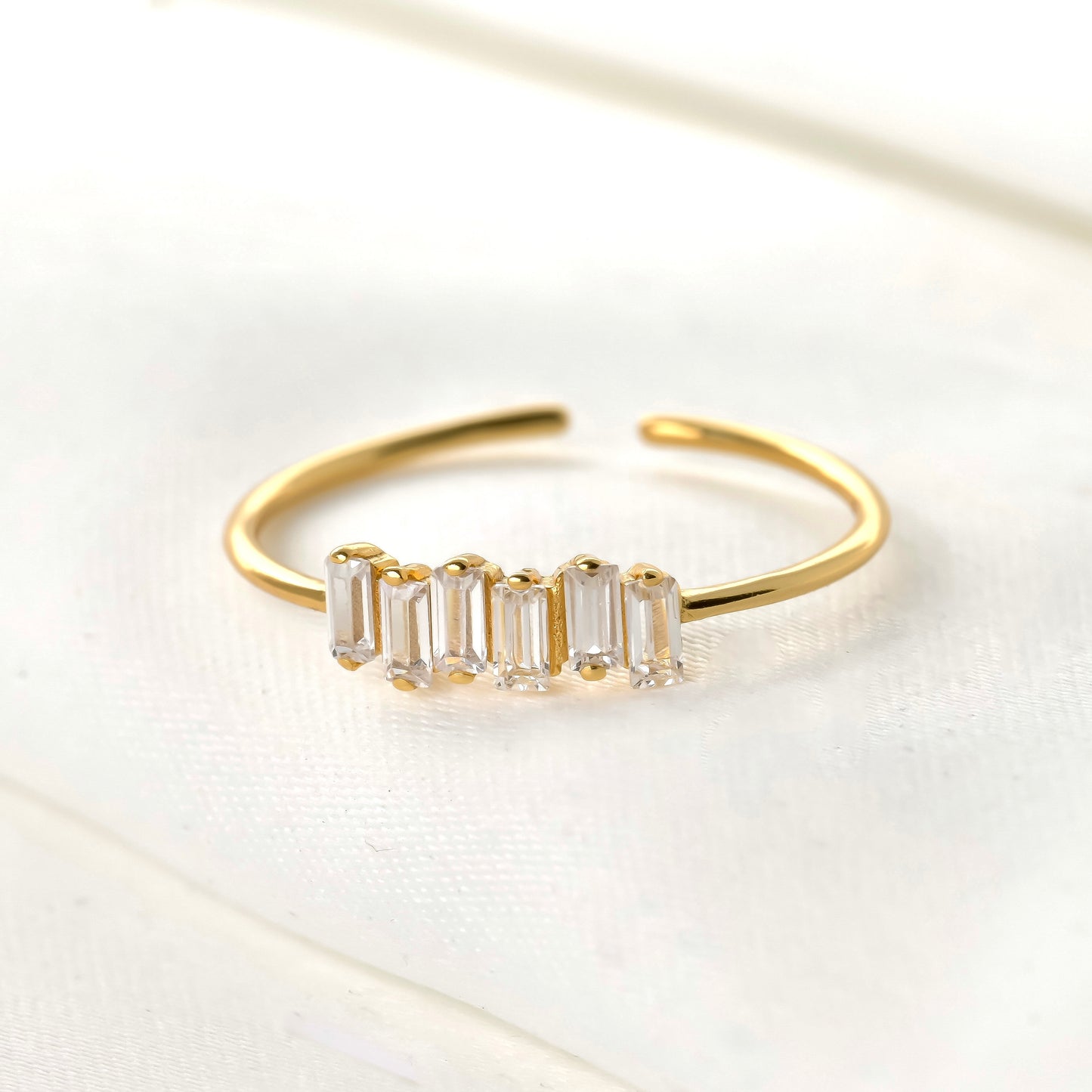 Gold open ring with 6 vertically set baguette cut stones on a light background