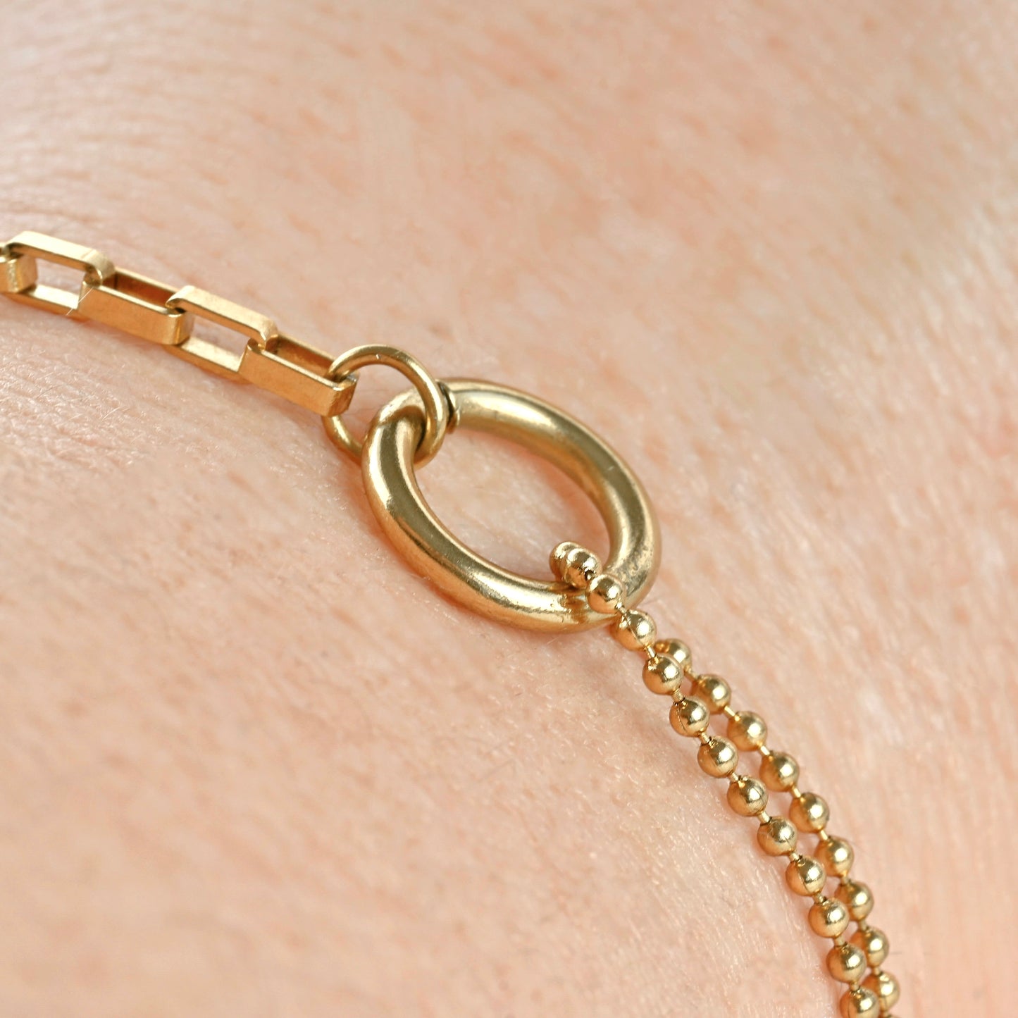 Close up view of the small circle linking the rectangular link chain and two layered ball chain on a wrist.