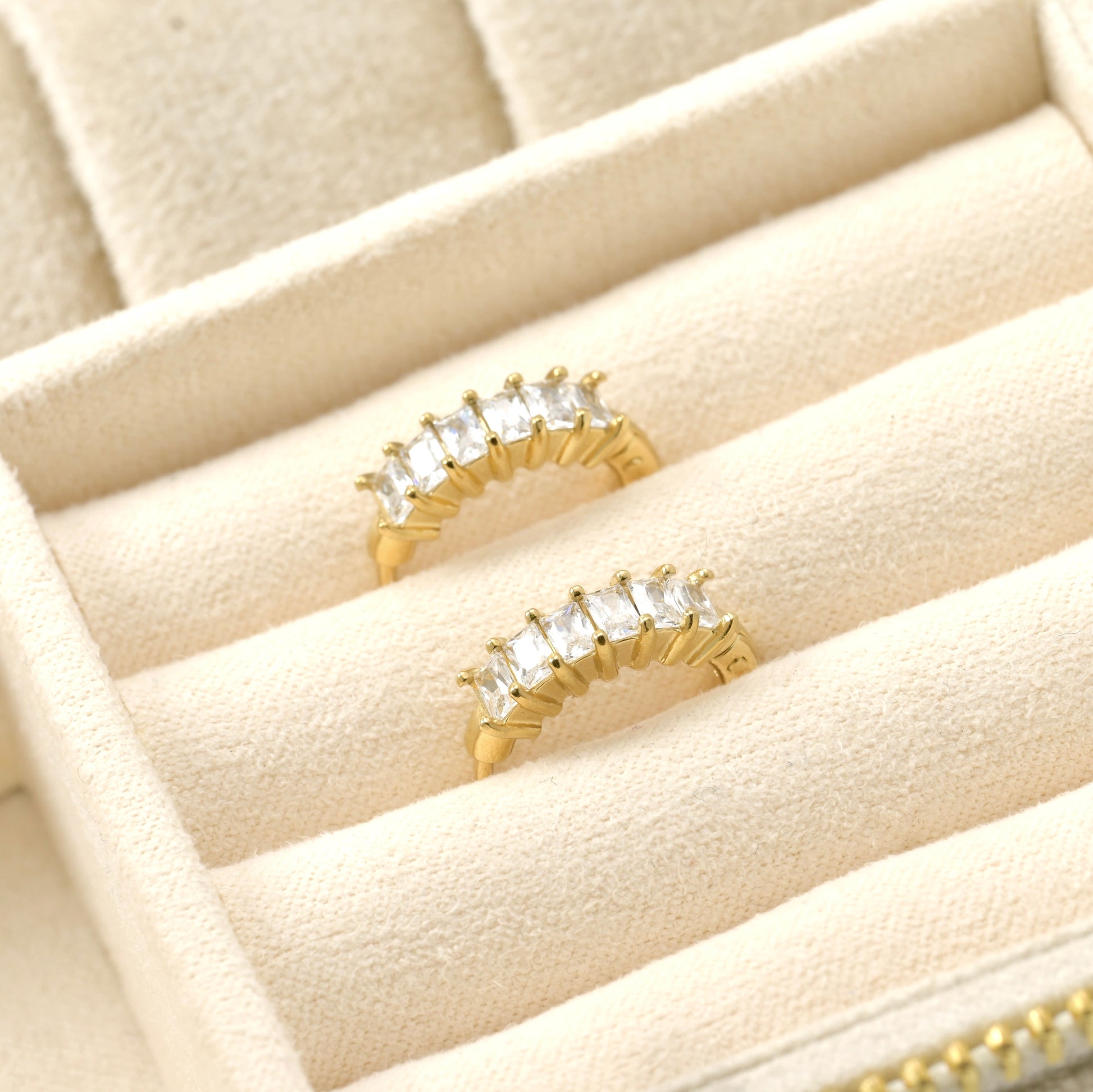 Gold clicker earrings with clear stones on a beige jewelry box