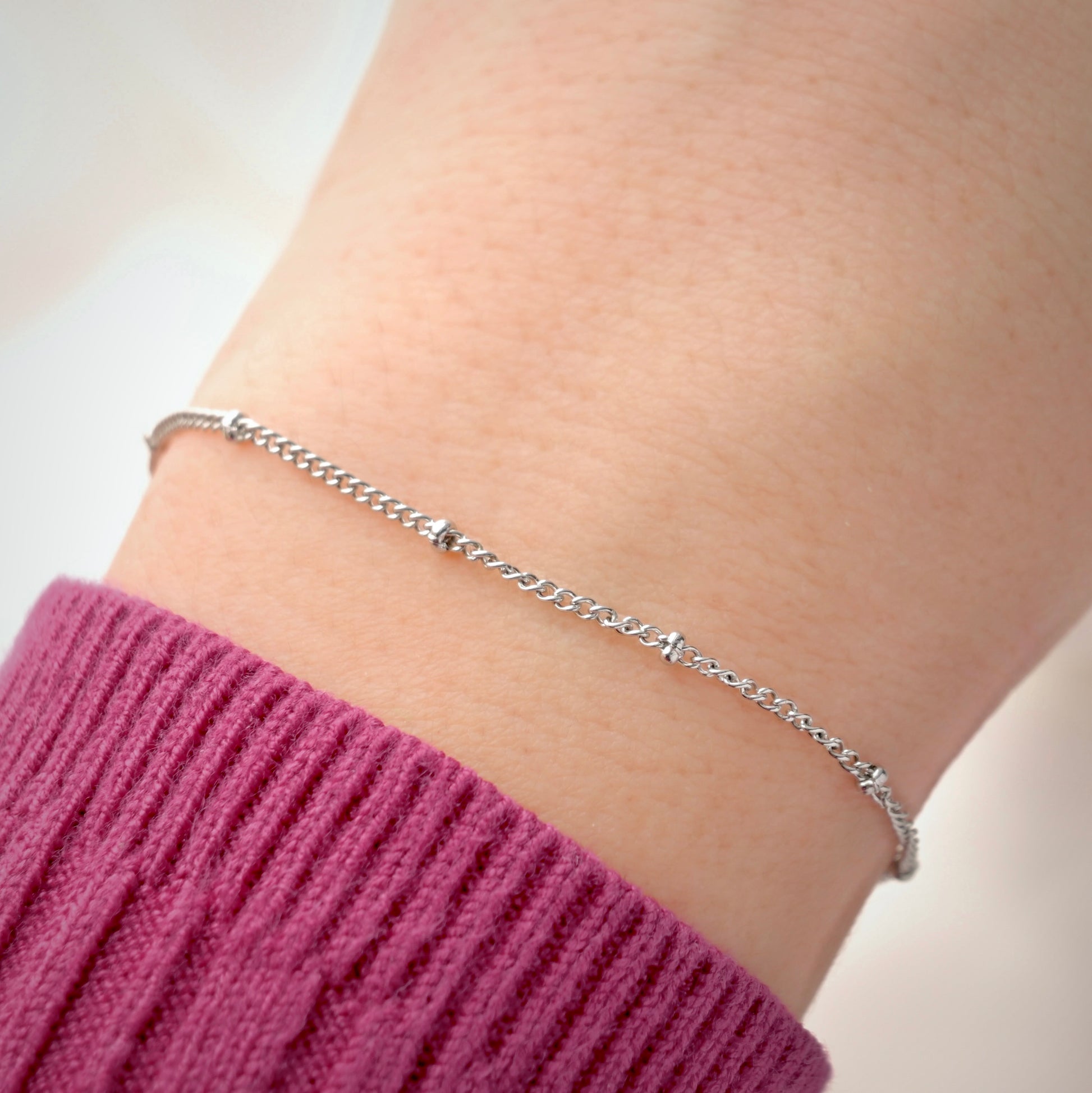 Silver satellite chain bracelet on a wrist with a blurred background