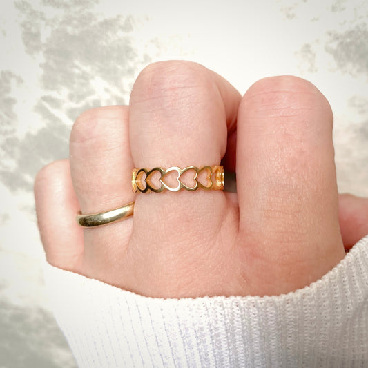 Gold ring with a heart link design worn on a finger against a white background