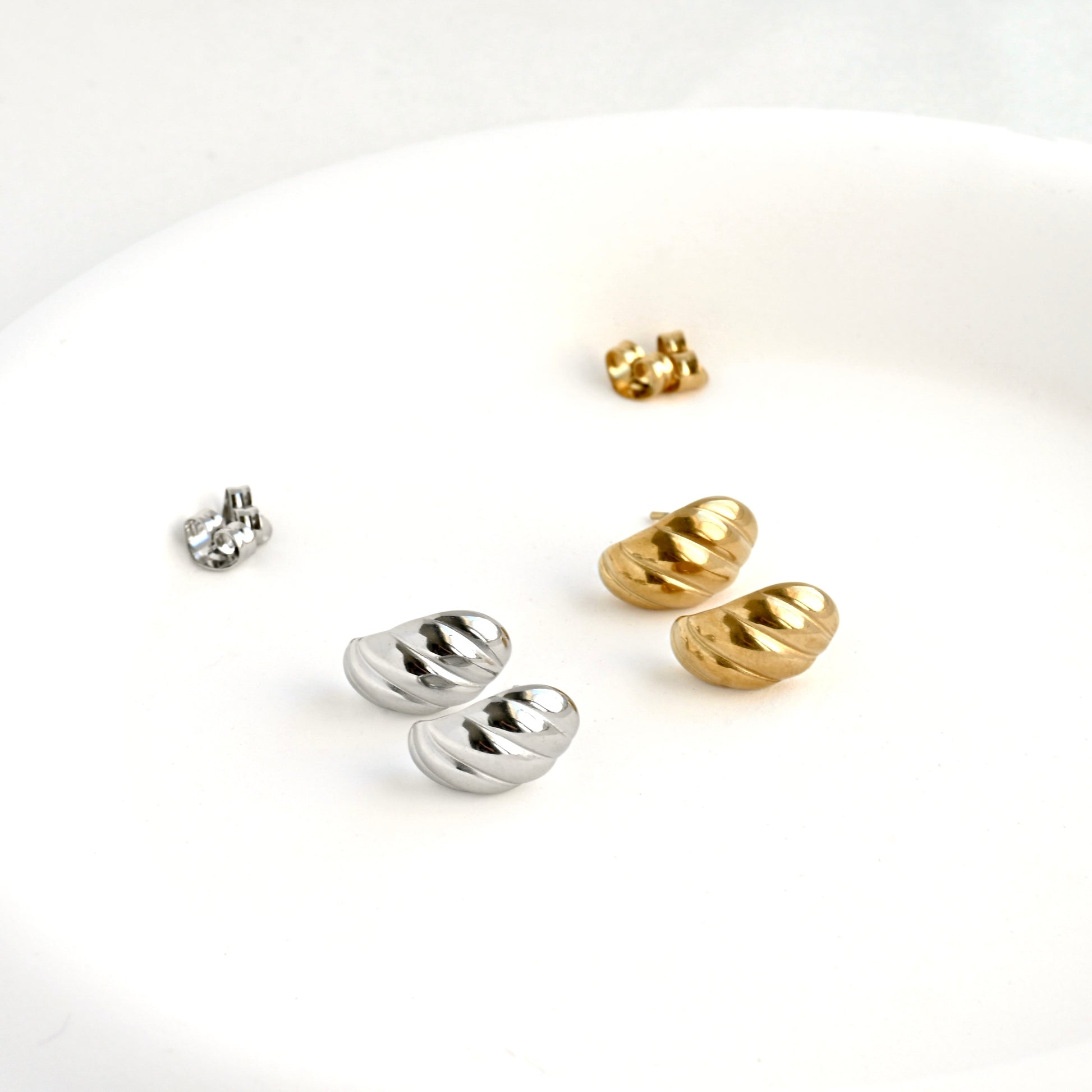 Pair of gold and silver small croissant huggies with butterfly backings at the back on a white background