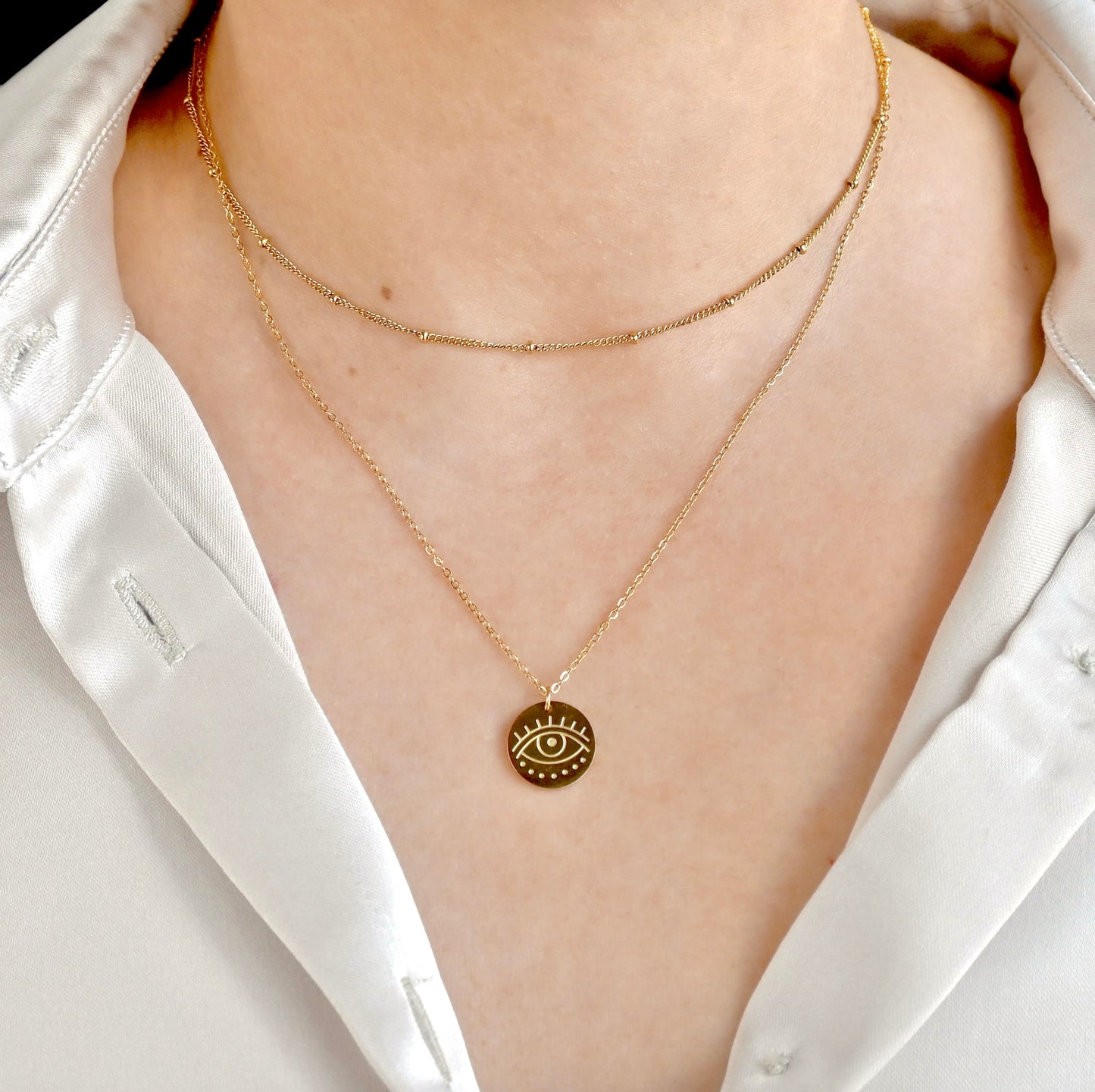 Double-layer gold necklace with a coin eye pendant on an 18 in long cable chain and a 14 in satellite chain, worn by a person in a white shirt.