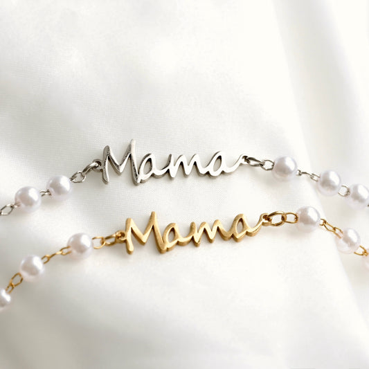 Two personalized pearl necklace spelling 'Mama' in cursive script, one in silver and one in gold, both adorned with white pearl beads and resting on a white satin background.