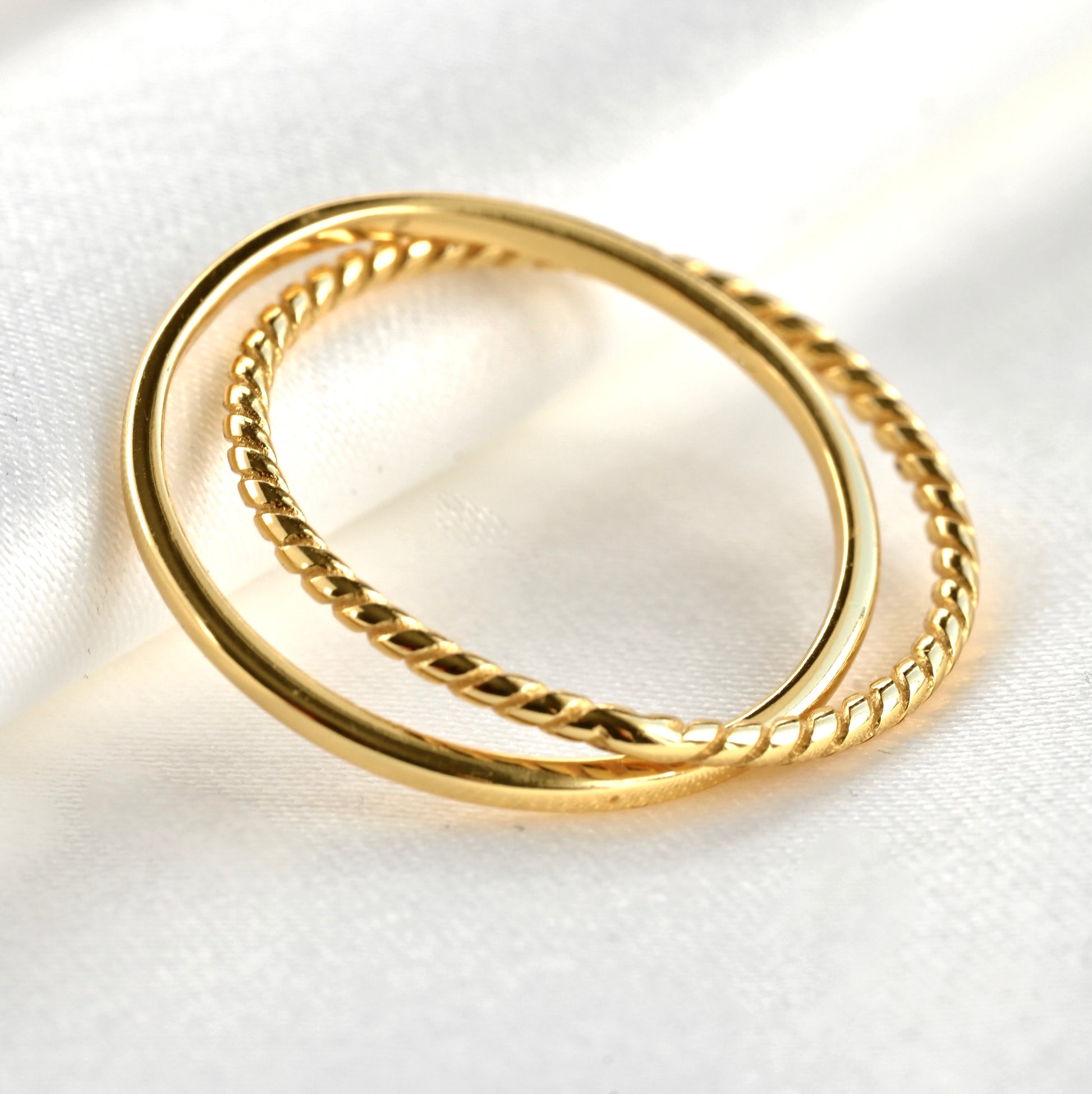 Close up view of textured gold criss cross ring  leaning against white fabric background