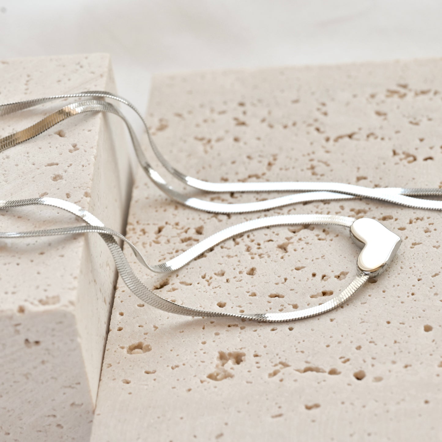 Silver heart jewelry on a textured beige surface