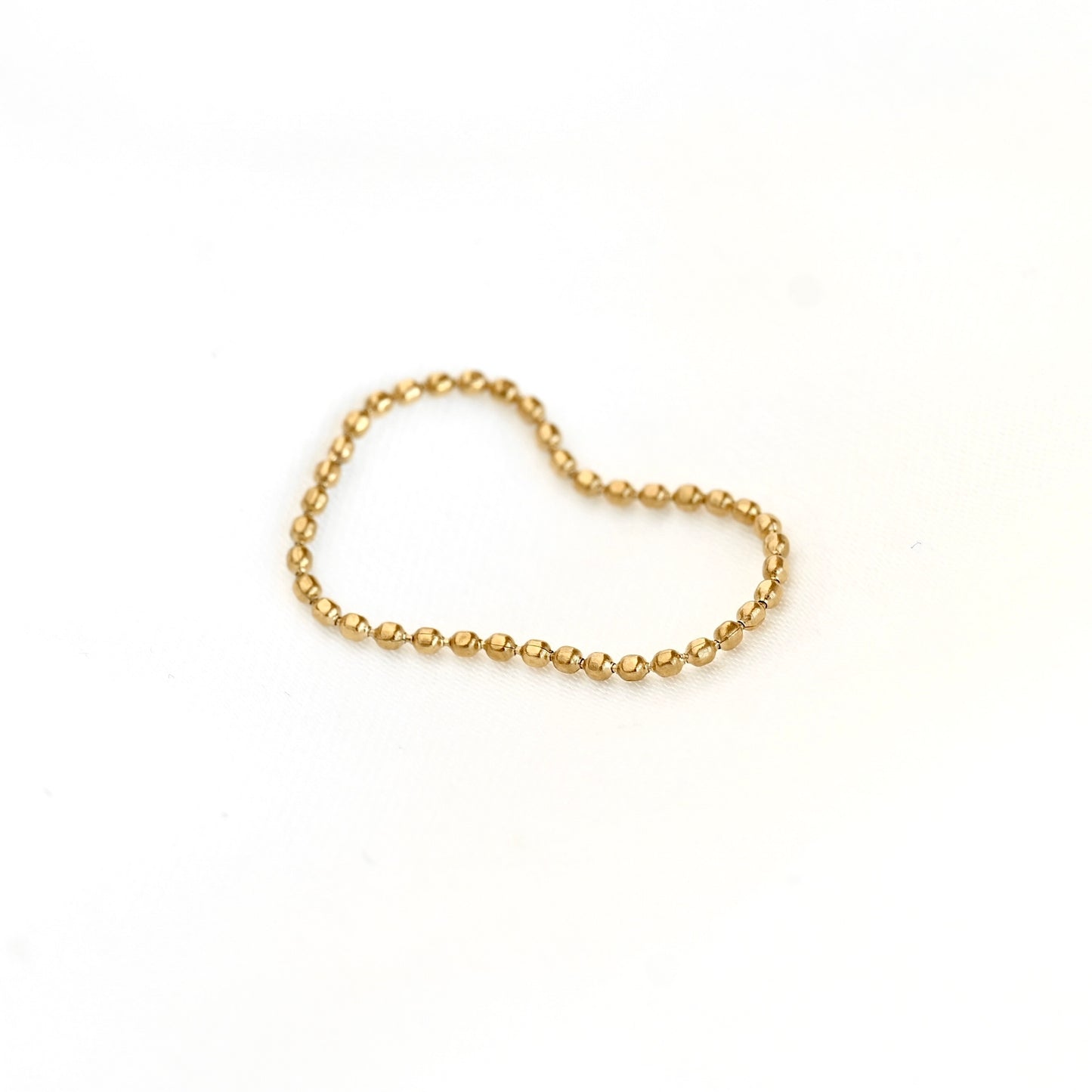 A delicate gold beaded chain ring arranged in a heart shape on a plain white background.