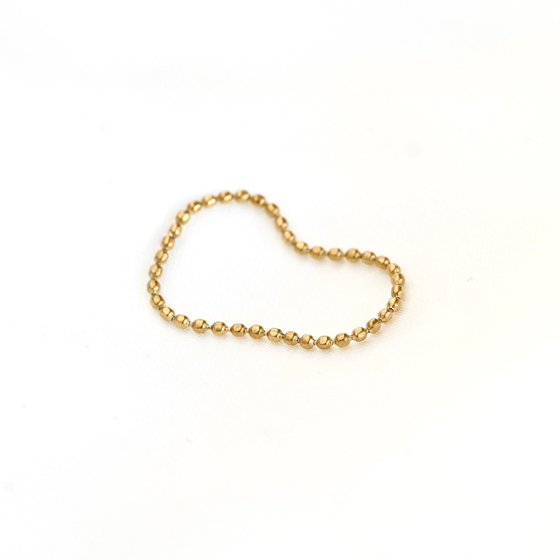 A delicate gold beaded chain ring arranged in a heart shape on a plain white background.
