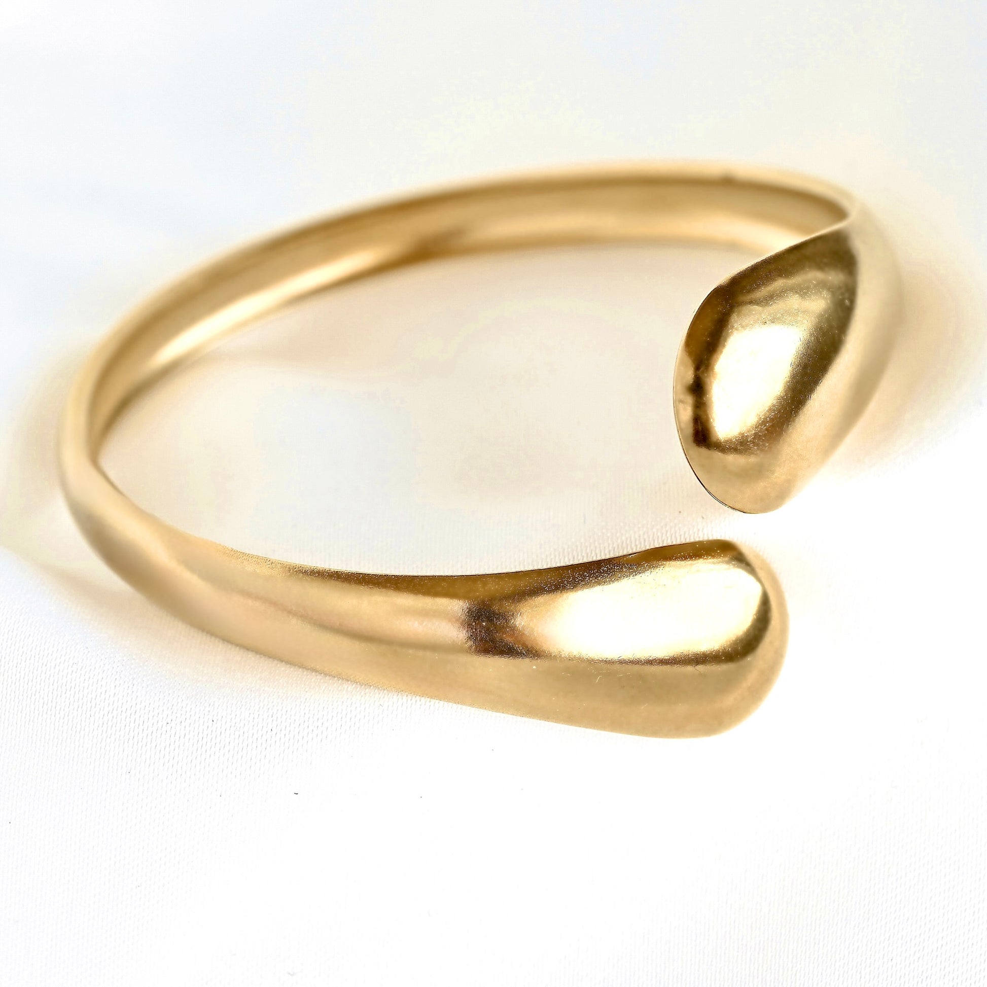A polished gold-tone open cuff ring with a smooth, organic teardrop-shaped end, photographed on a clean white background.